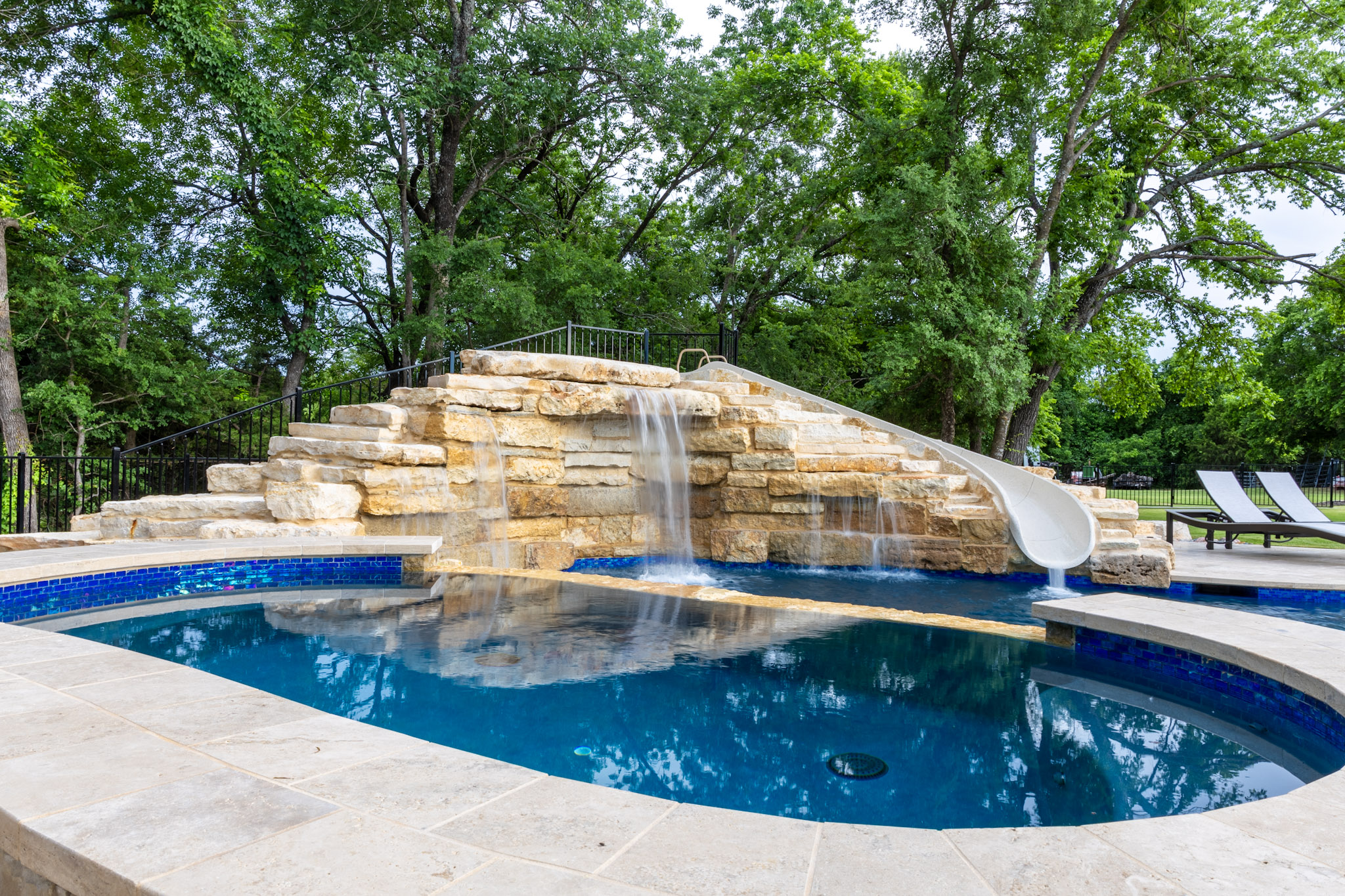 Custom resort-style pool with natural stone waterfall, integrated slide and spa in Weston, TX
