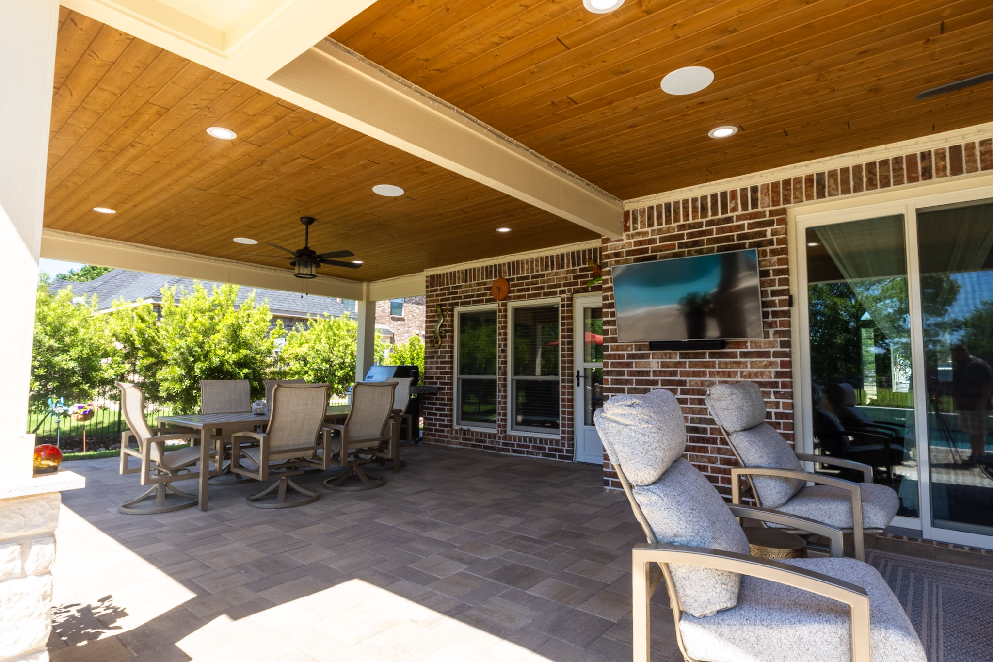 Covered patio with wood ceiling, dining table, lounge chairs, ceiling fan and mounted television.