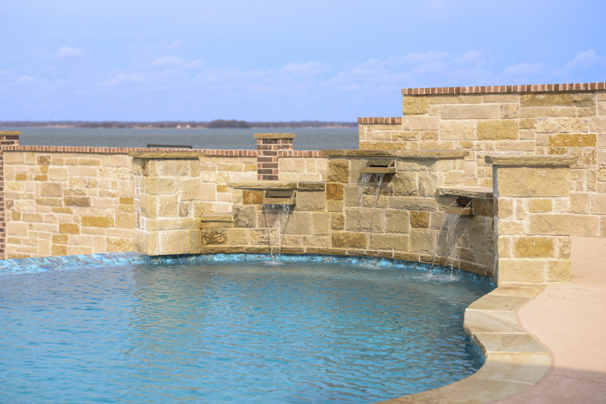 Pool with three stone sheer descents and a lake visible behind the masonry wall.