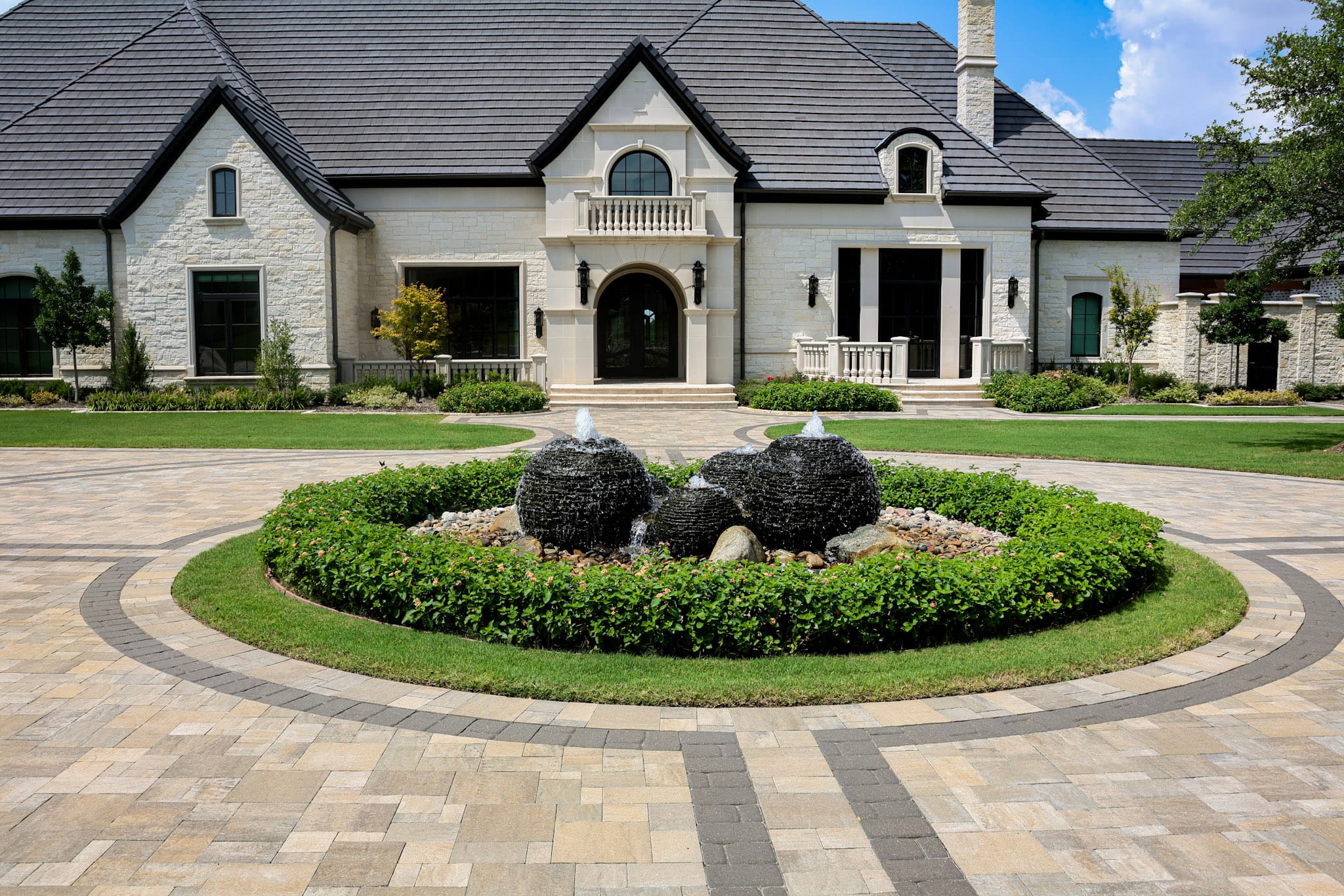 Belgard paver circular driveway with landscaped fountain in front of a large Allen custom home.