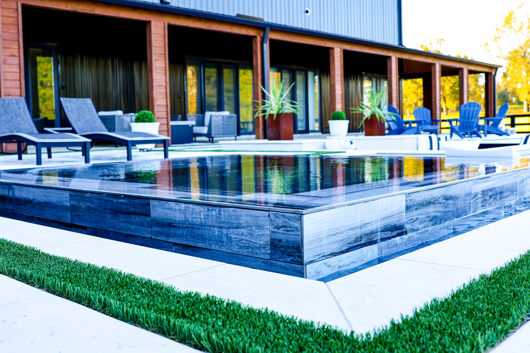 Raised square spa with dark gray stone finish beside a modern swimming pool in Troup, Texas.