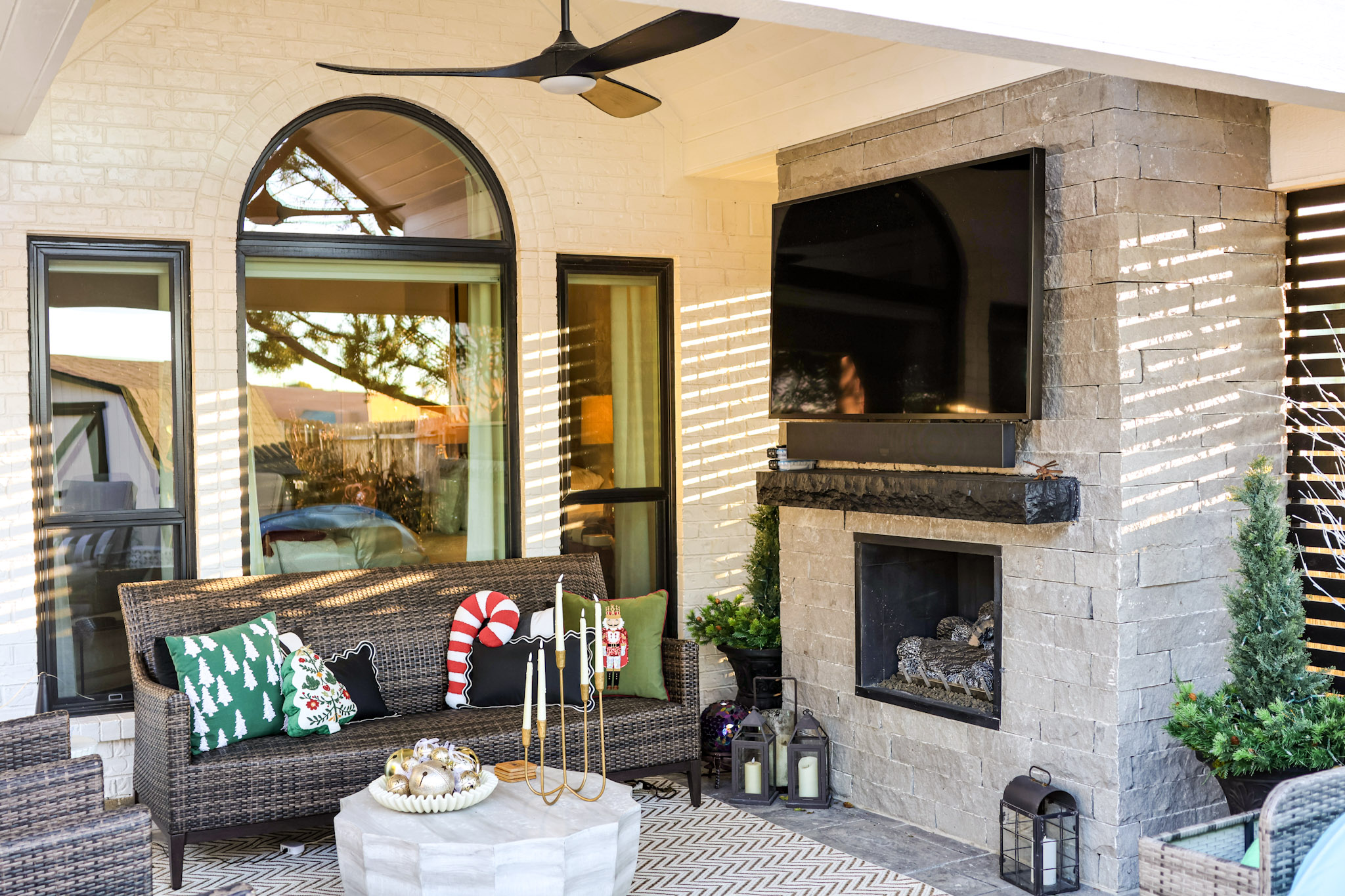 Covered patio with stone fireplace, mounted television, ceiling fan and wicker seating.