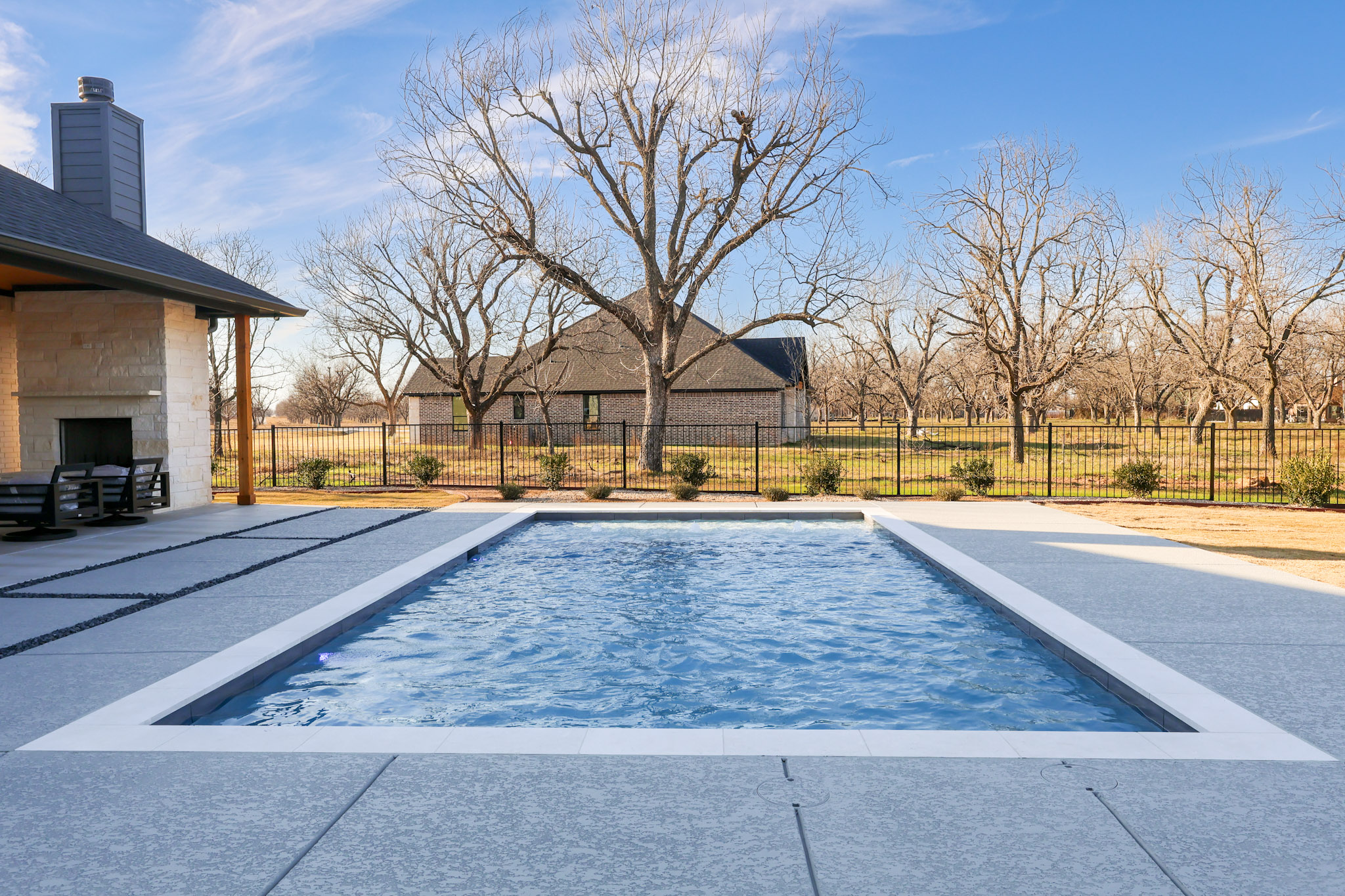 Rectangular swimming pool with light coping and textured concrete deck in a fenced backyard.