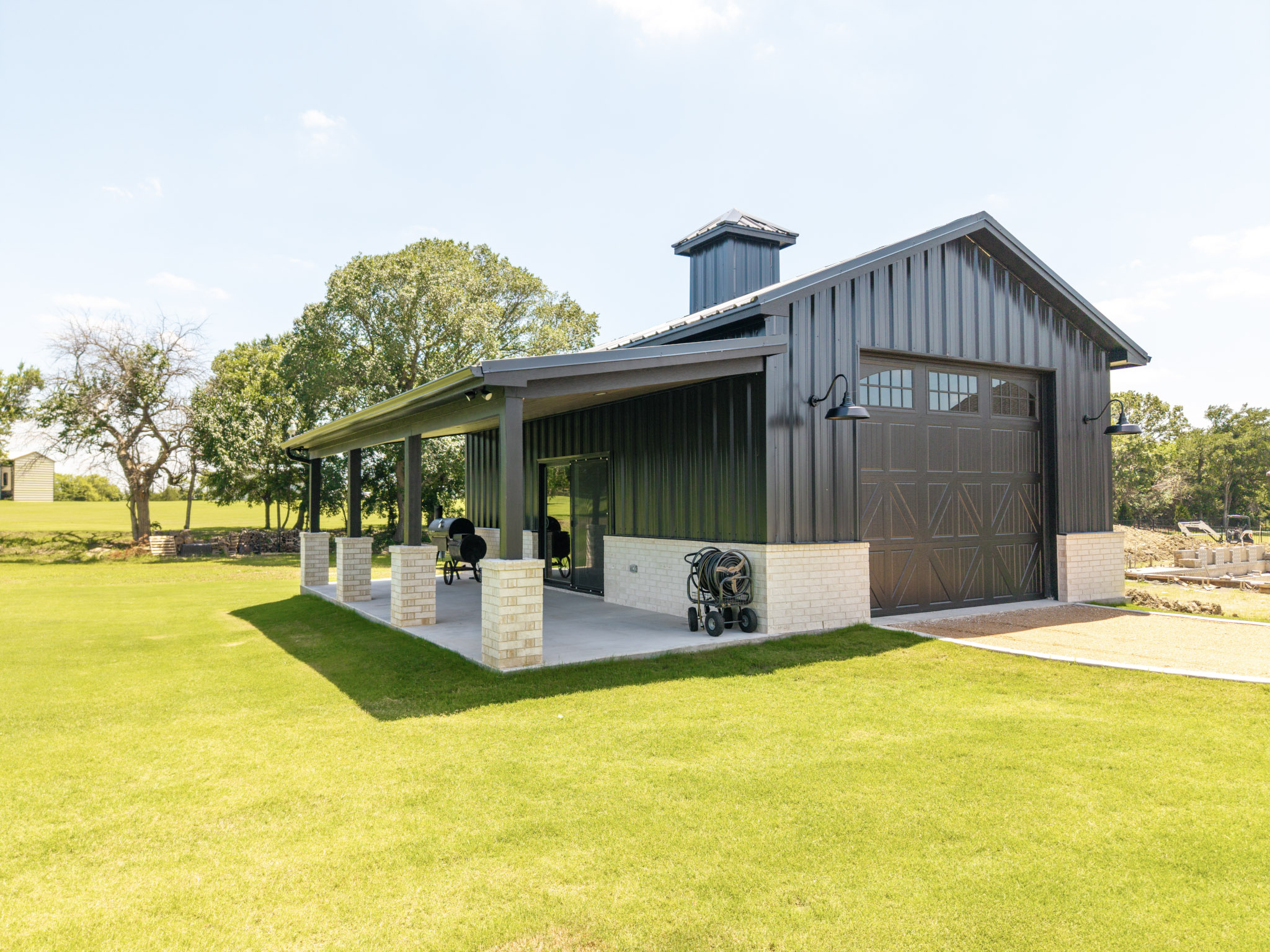 Dark metal custom barn with covered side patio, masonry accents and large overhead door in Van Alstyne.