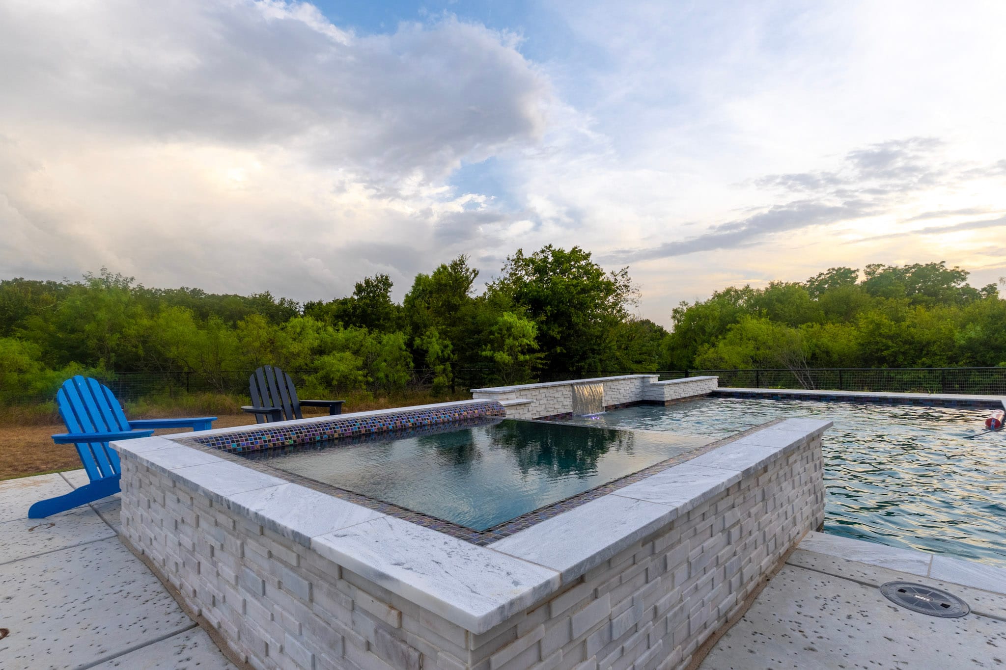 Raised stone spa beside a custom swimming pool with wooded views in Paradise, Texas.