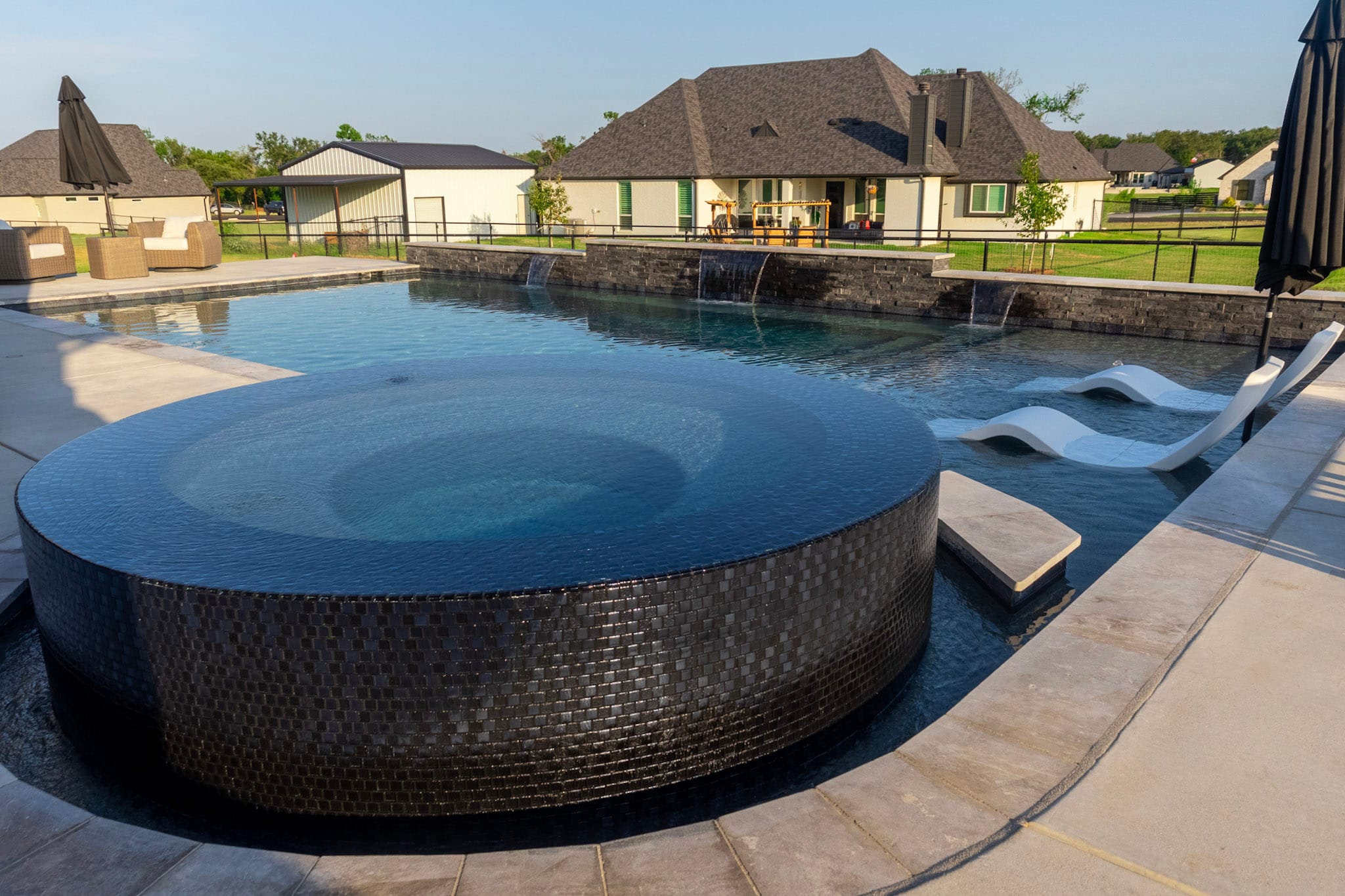 PTX Custom Pools project in Springtown with a raised circular spa, tanning ledge and dark stone water feature wall.