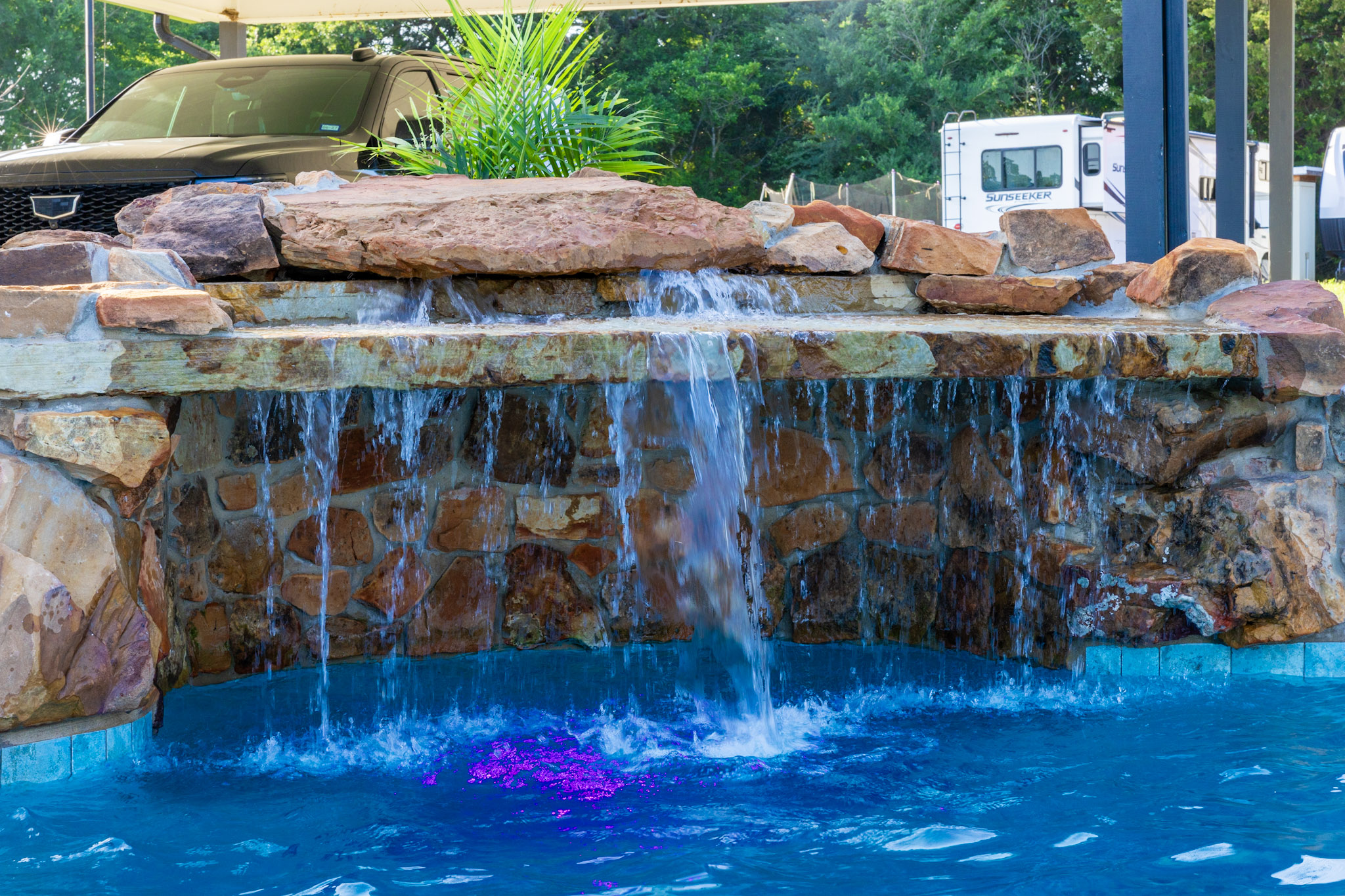 Natural stone waterfall with multiple cascades flowing into a blue pool with purple lighting.
