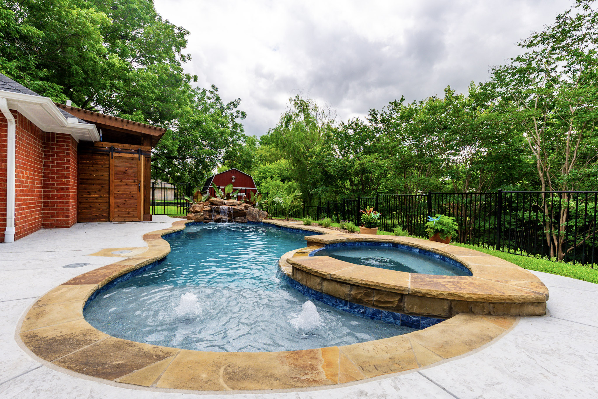 Freeform pool with raised spa, two bubblers and rock waterfall in a landscaped backyard.