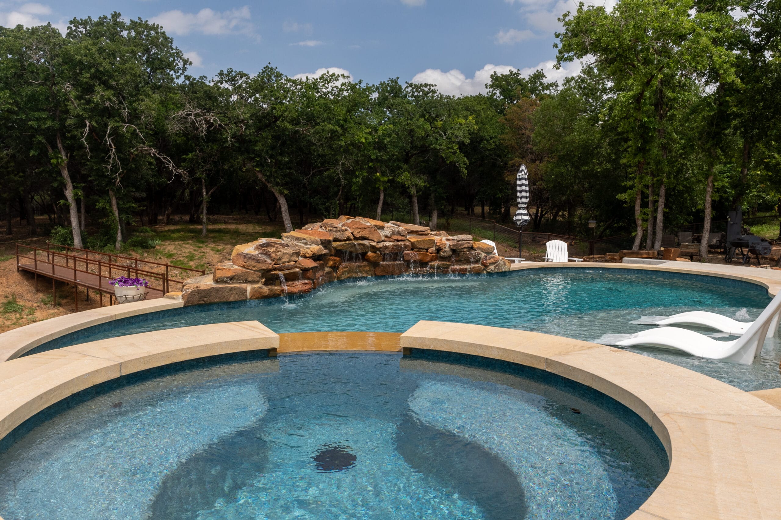 Raised circular spa overlooking a freeform Weatherford pool with rock waterfall and two in-pool loungers.