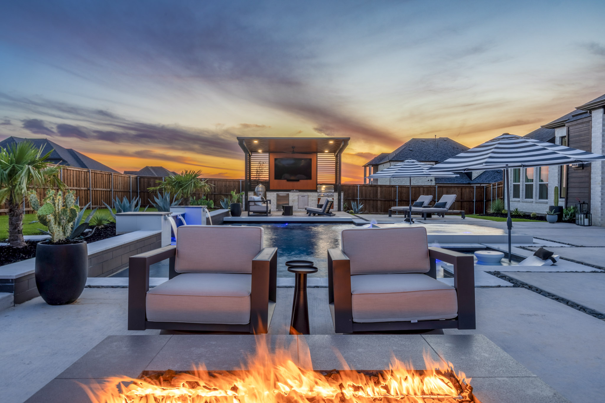 Luxury backyard fire pit overlooking modern swimming pool at sunset in Rockwall, TX.