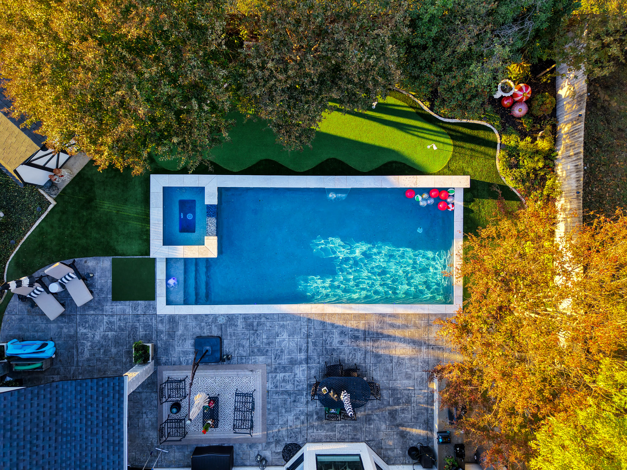Top-down aerial of rectangular pool, raised spa, putting green and large backyard patio.