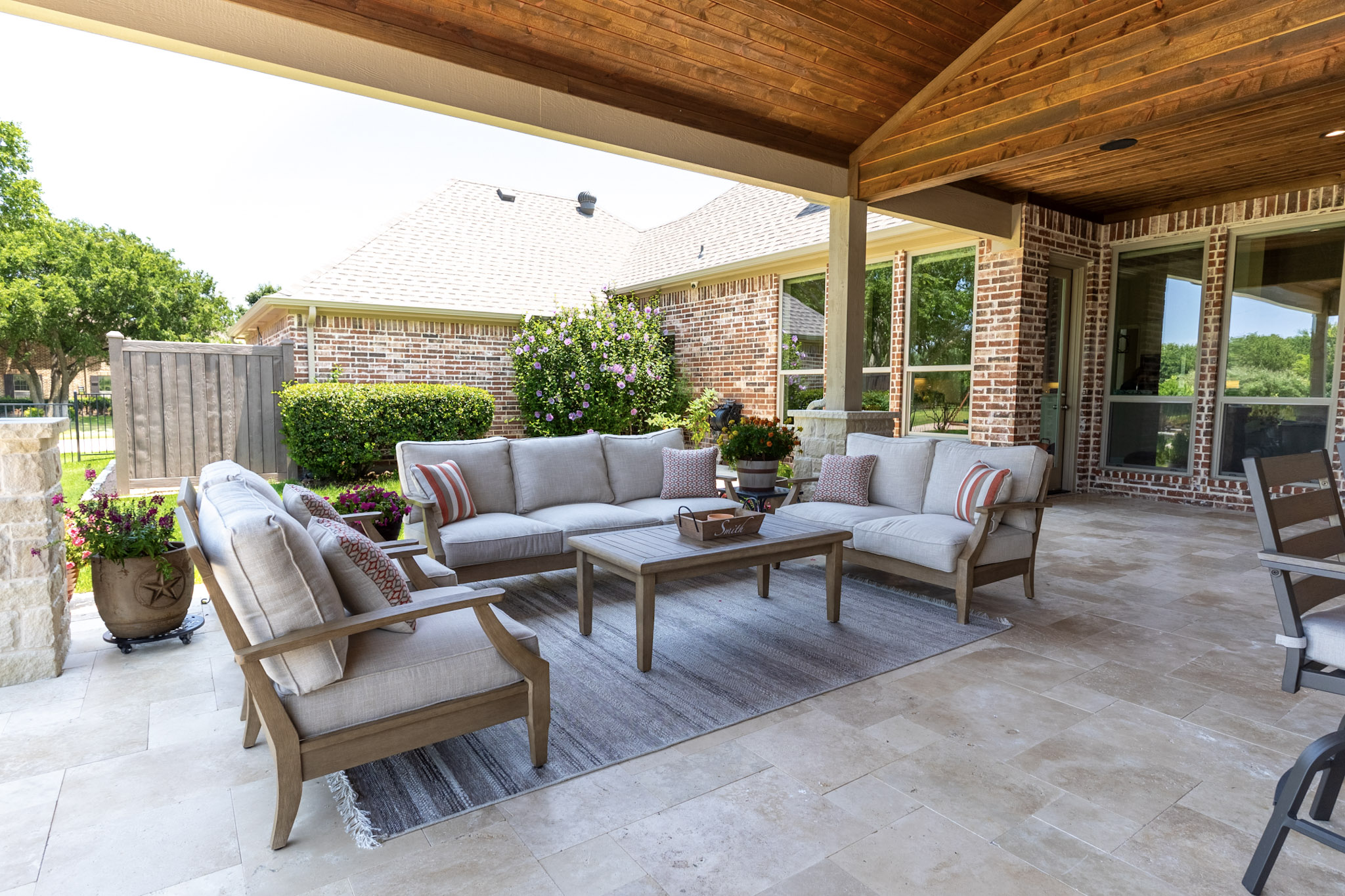 Covered outdoor seating area with sofas, chairs, travertine flooring, and stained wood ceiling.