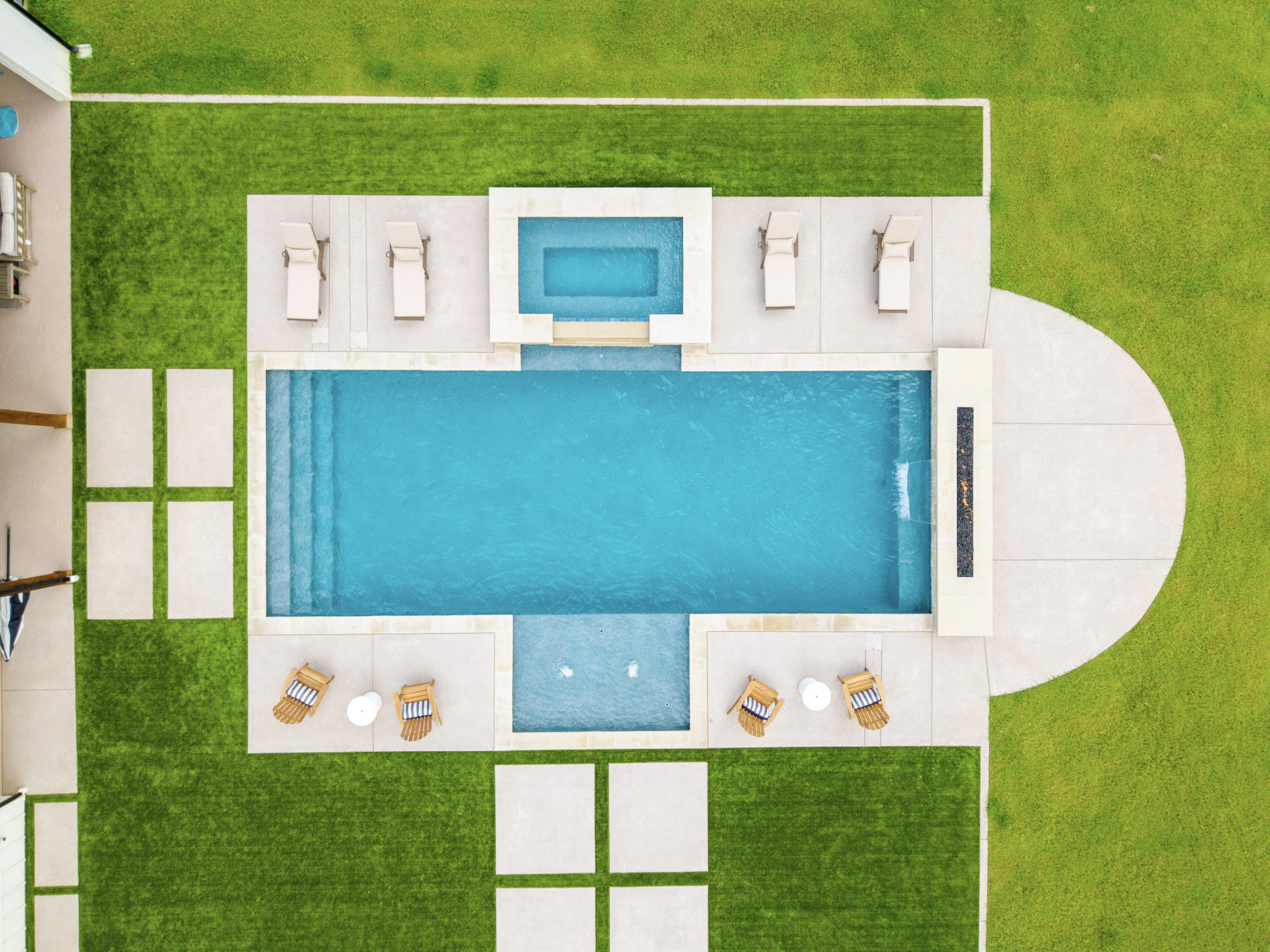 Top-down drone view of custom pool with raised spa, tanning ledge, fire feature and surrounding lawn.