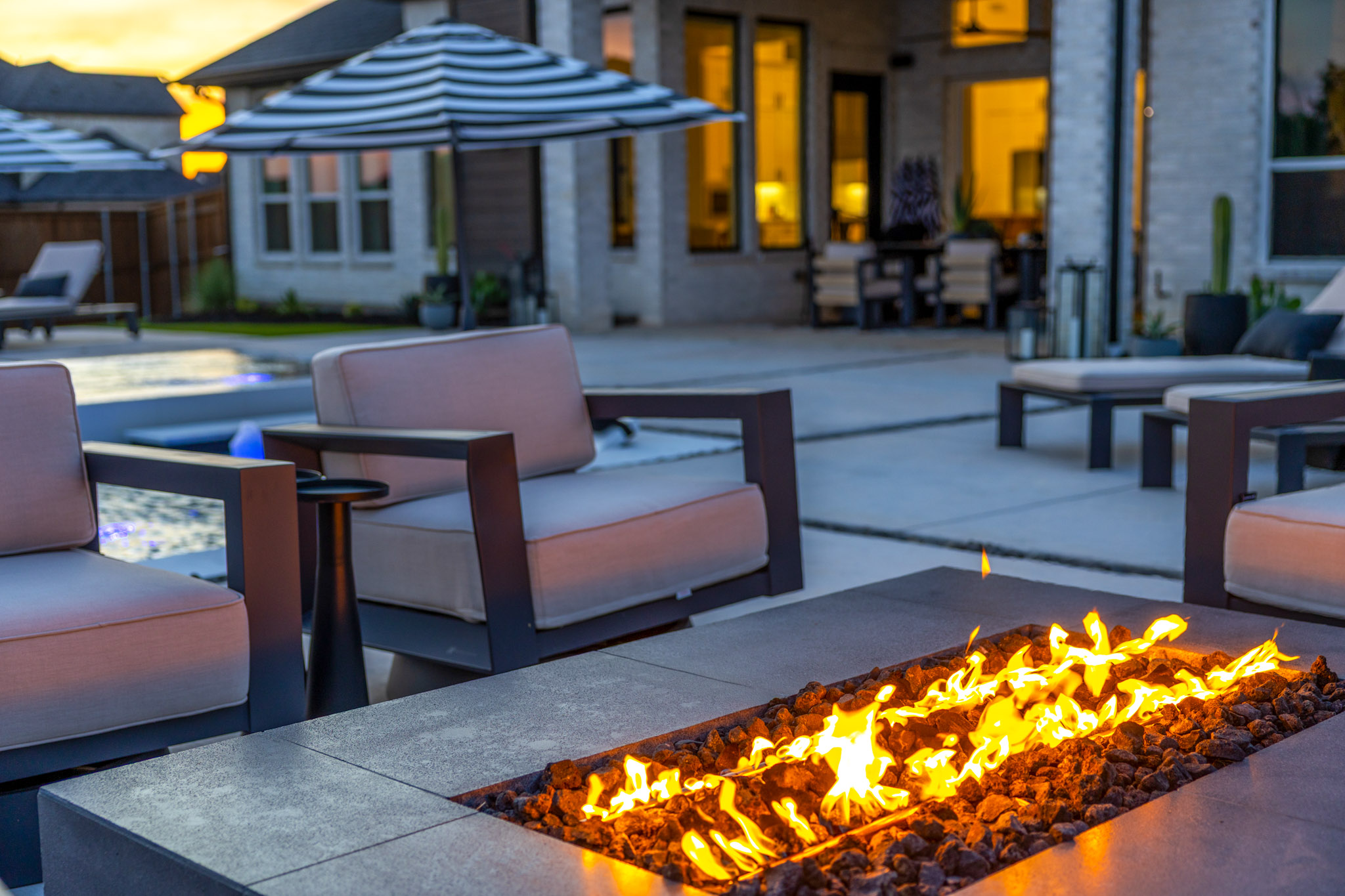 Modern linear gas fire feature surrounded by outdoor lounge seating beside a swimming pool.