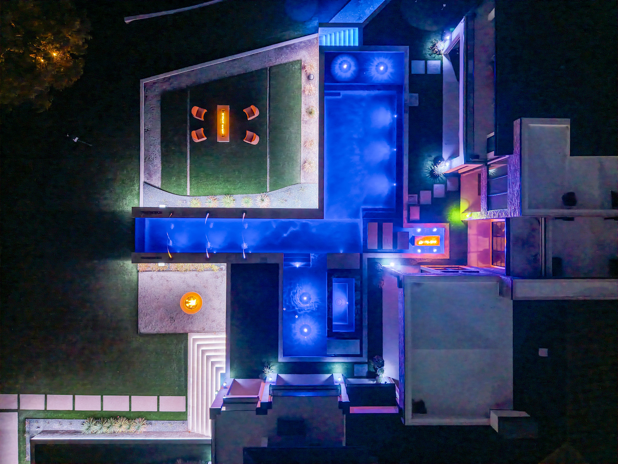Overhead night drone view of luxury pools, spa and fire lounge.