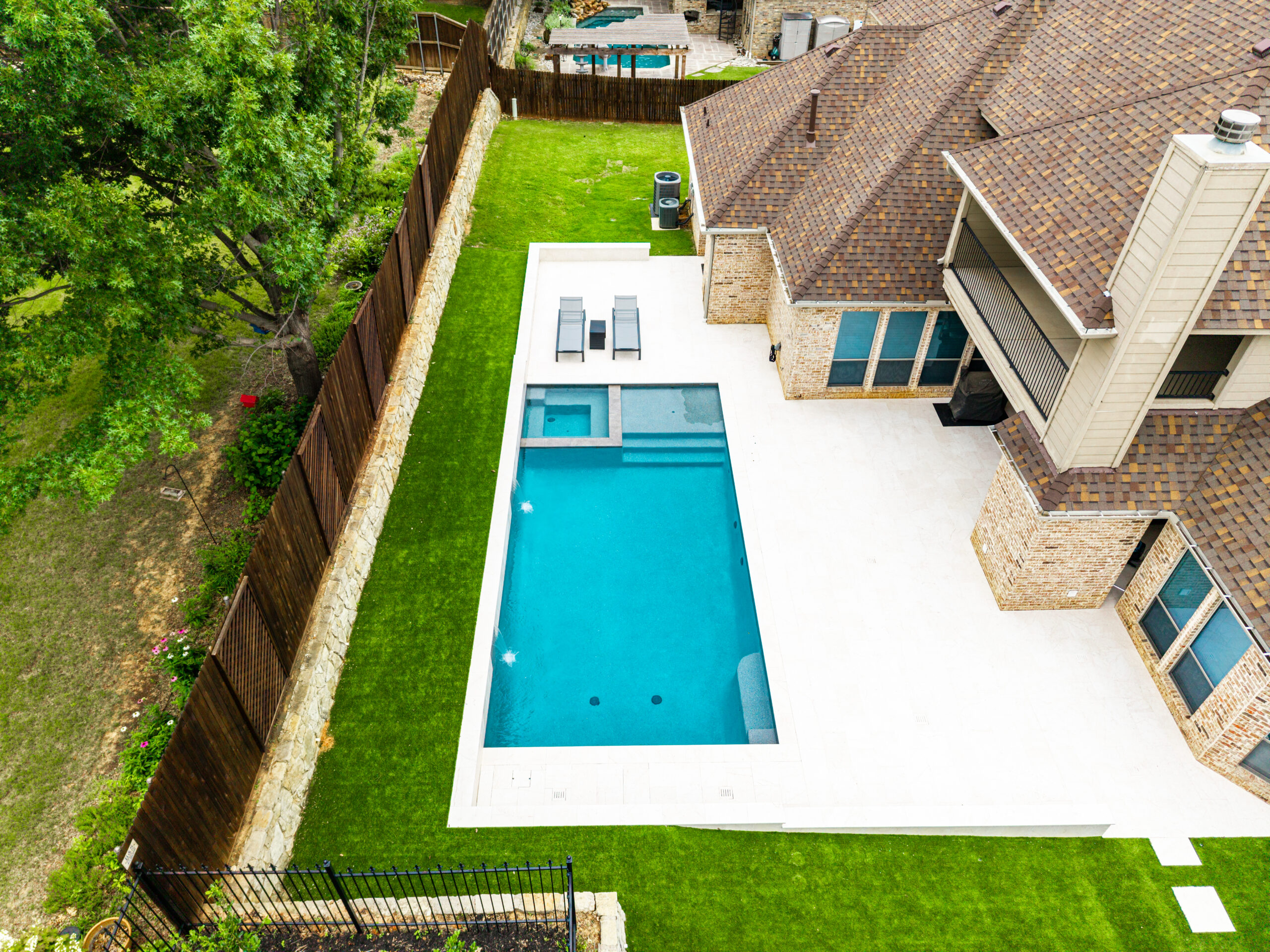 Integrated spa overlooking modern swimming pool with dual sheer descent water features in Colleyville, Texas.