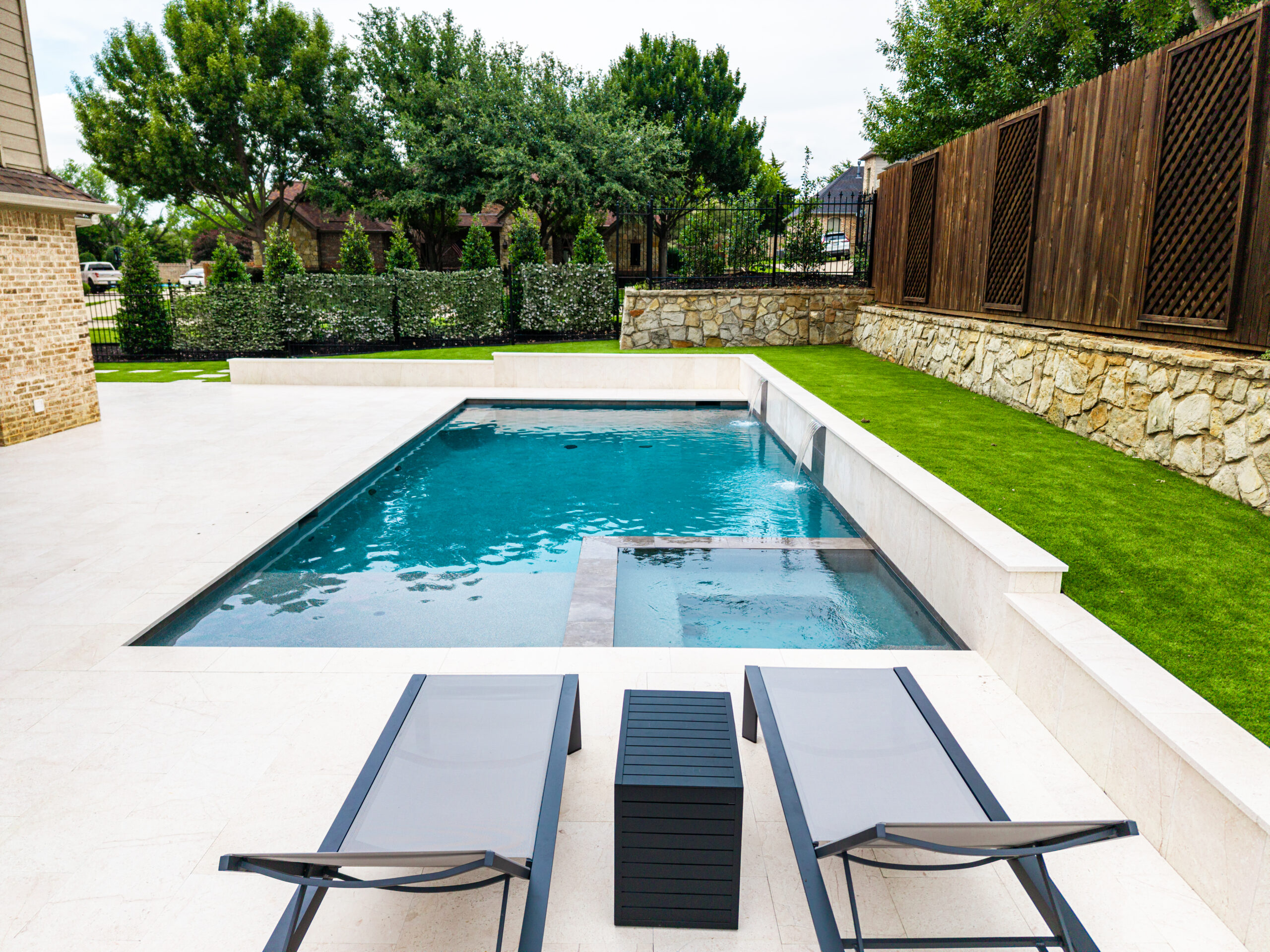 Dual sheer descent waterfalls flowing from a light stone pool wall at a modern Colleyville swimming pool.