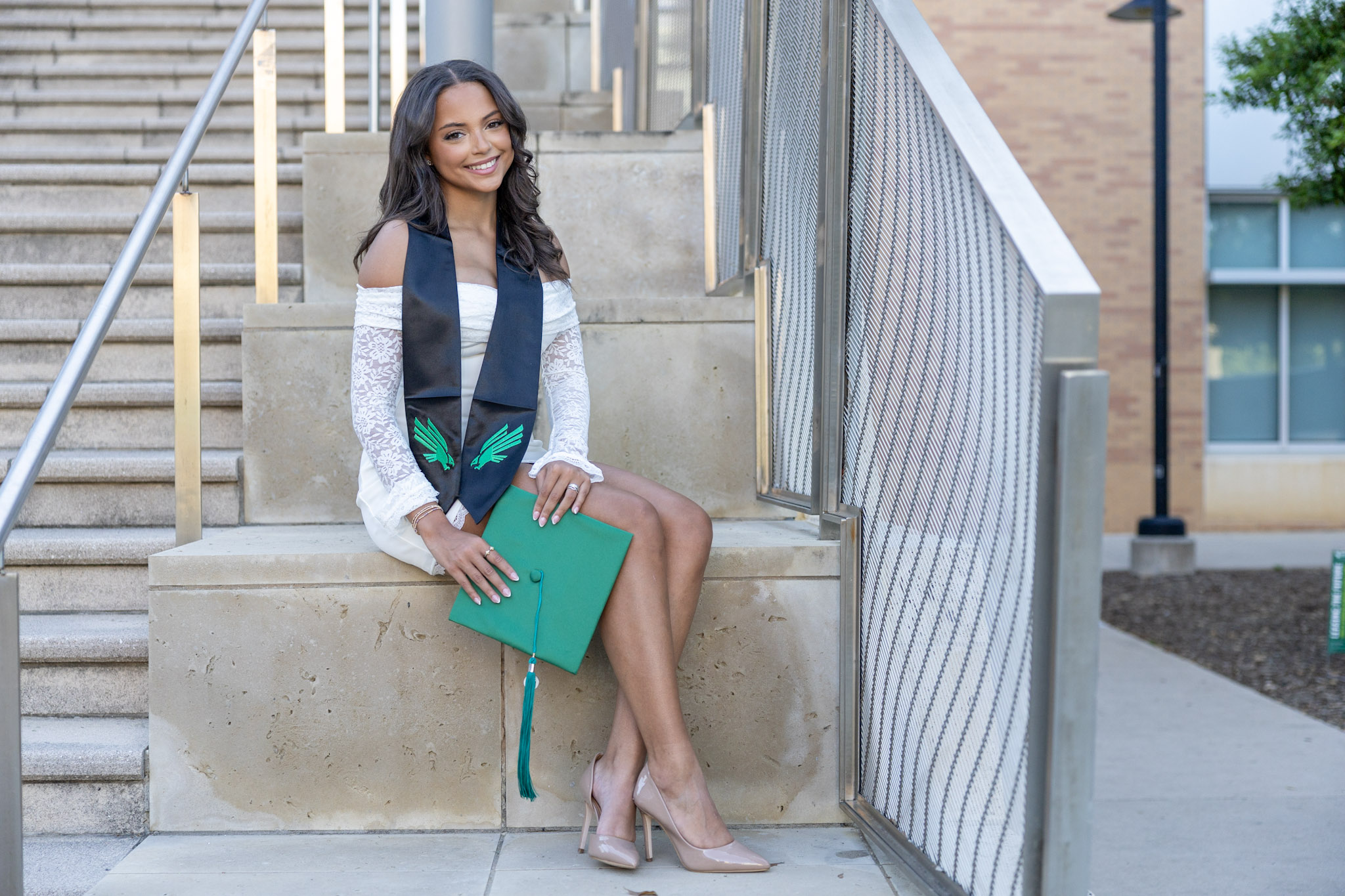 UNT graduate seated on stone steps holding a green graduation cap