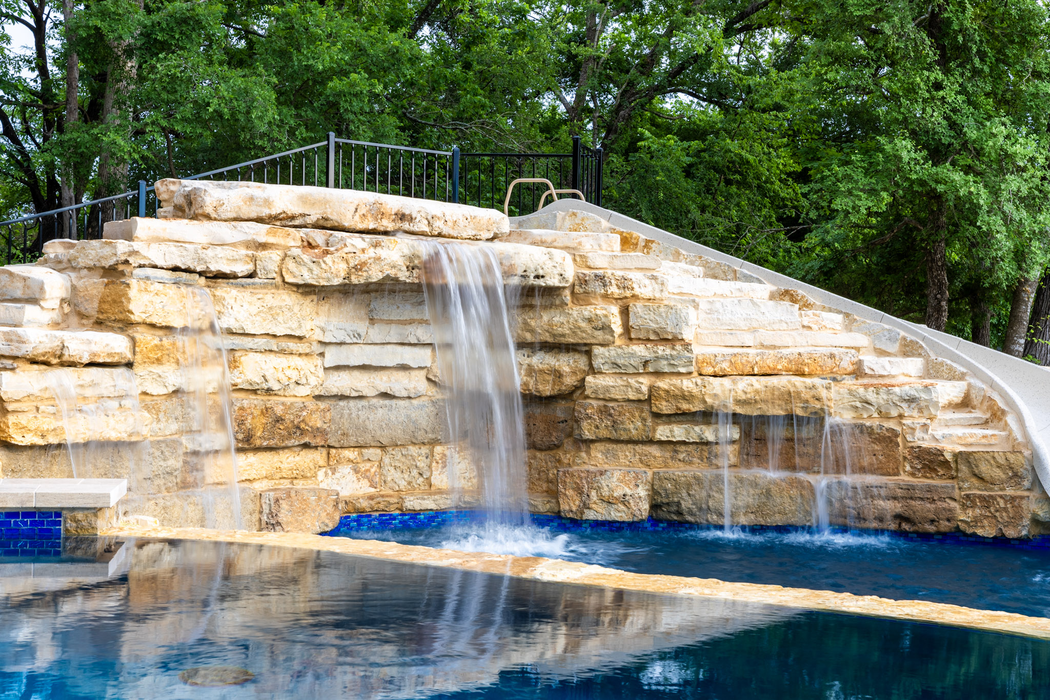 Natural stone pool waterfall and integrated slide at custom Weston, Texas landscape project