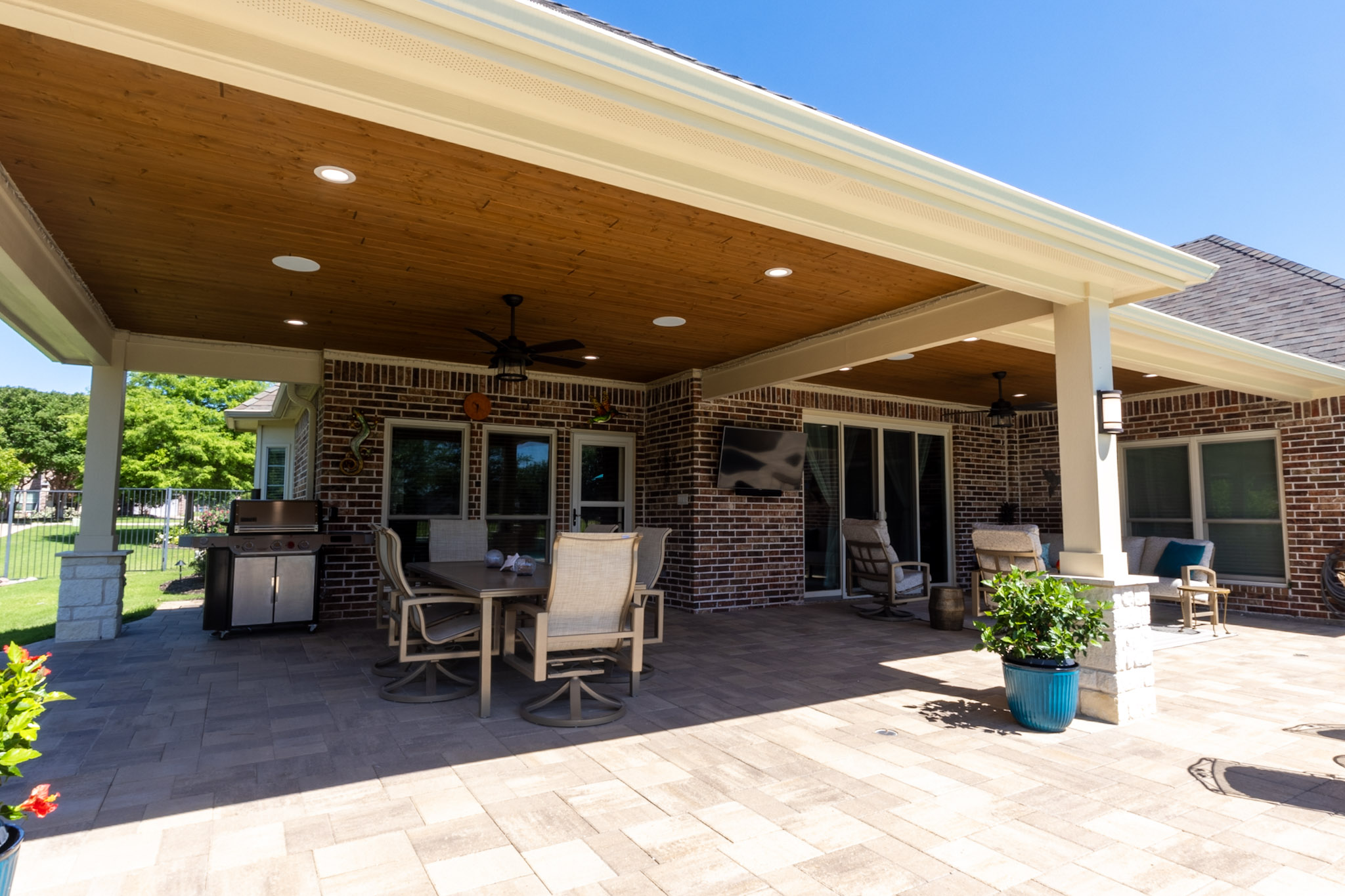 Extended covered patio with wood ceilings, stone-base columns, dining and lounge furniture.