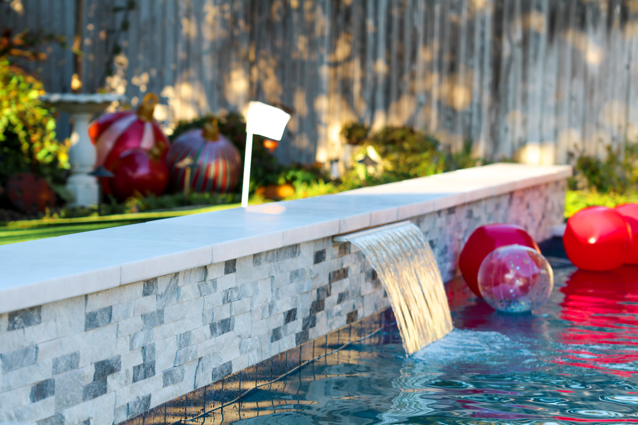 Wide sheer descent flowing from a stacked-stone pool wall into blue water.
