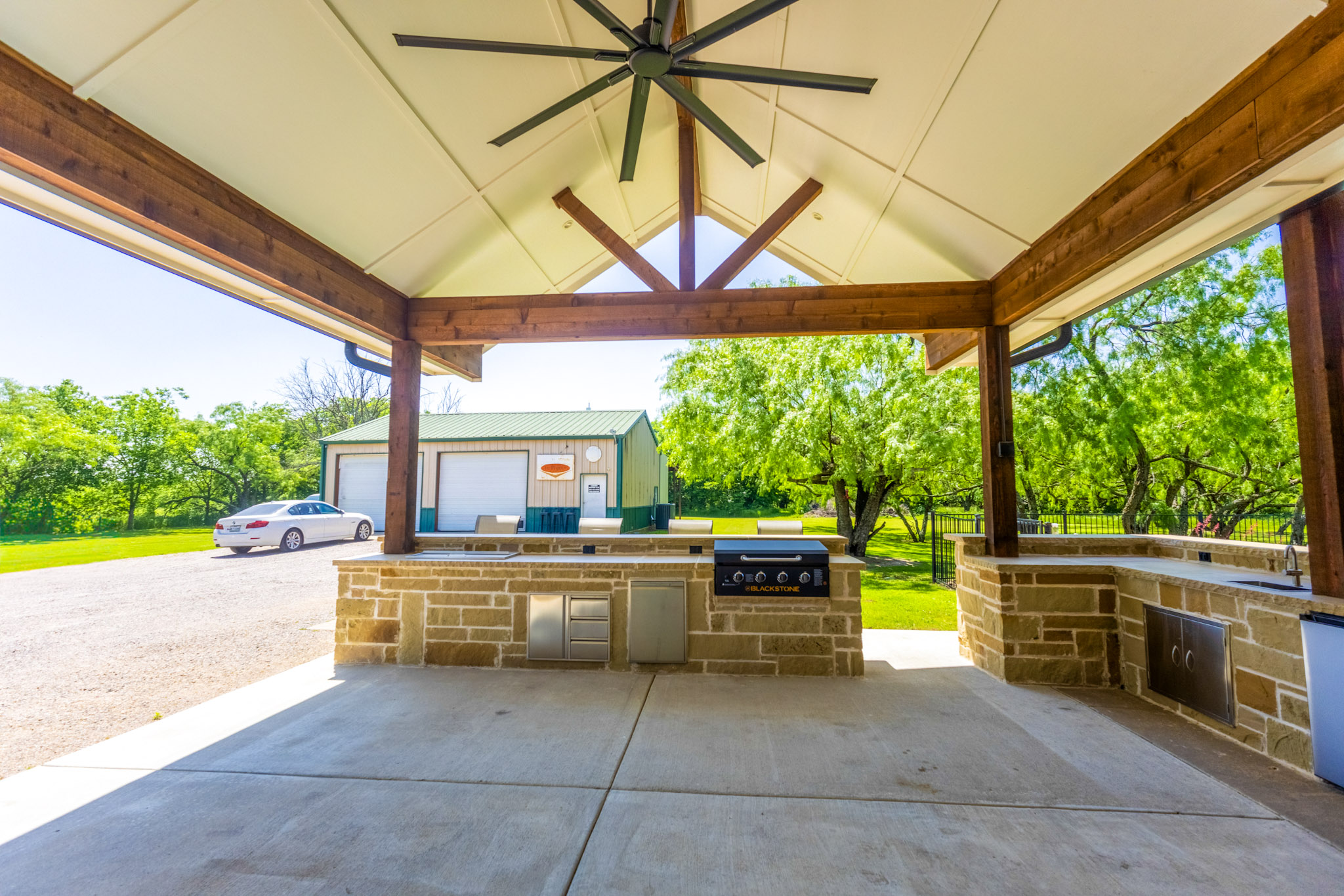 Covered stone outdoor bar with stools, exposed wood beams and vaulted white ceiling.