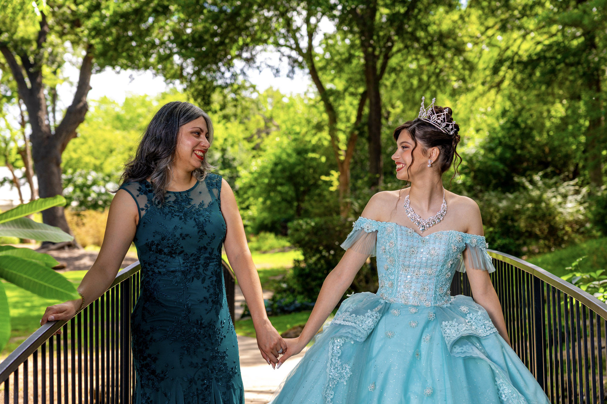 Mother and daughter holding hands on a garden bridge during a quinceañera session