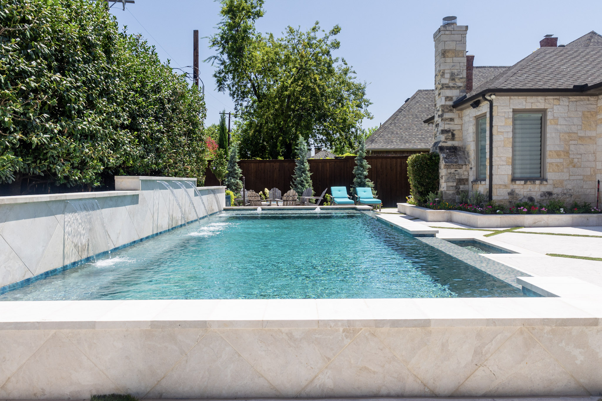 Custom swimming pool with raised water features and stone home in University Park, TX
