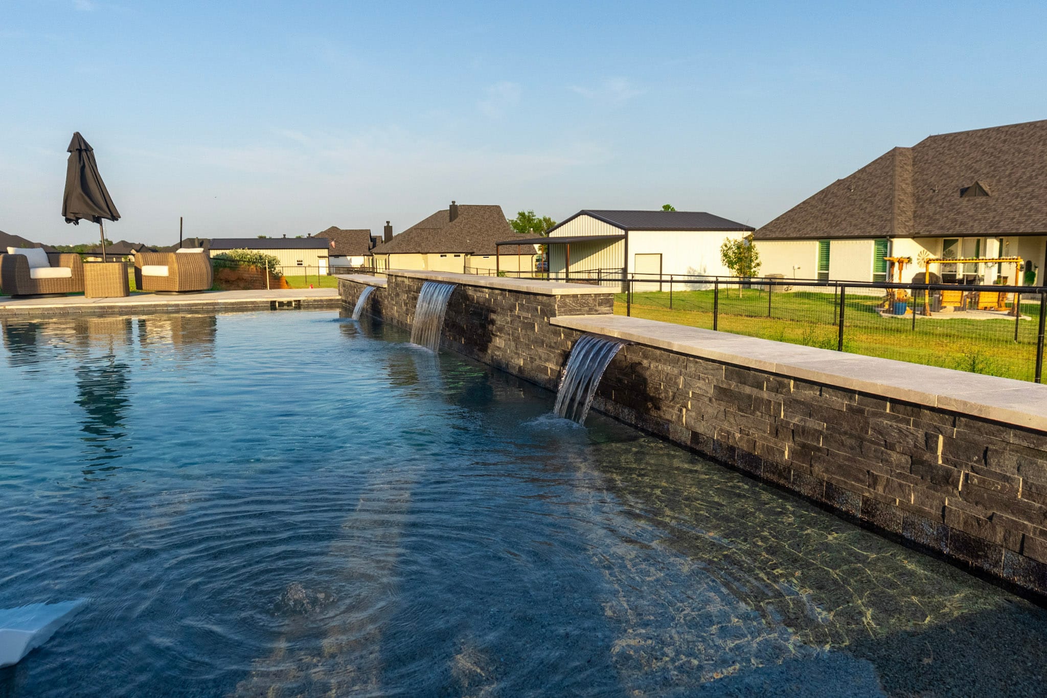 Dark stacked-stone pool wall with three sheer descents flowing into a Springtown swimming pool.