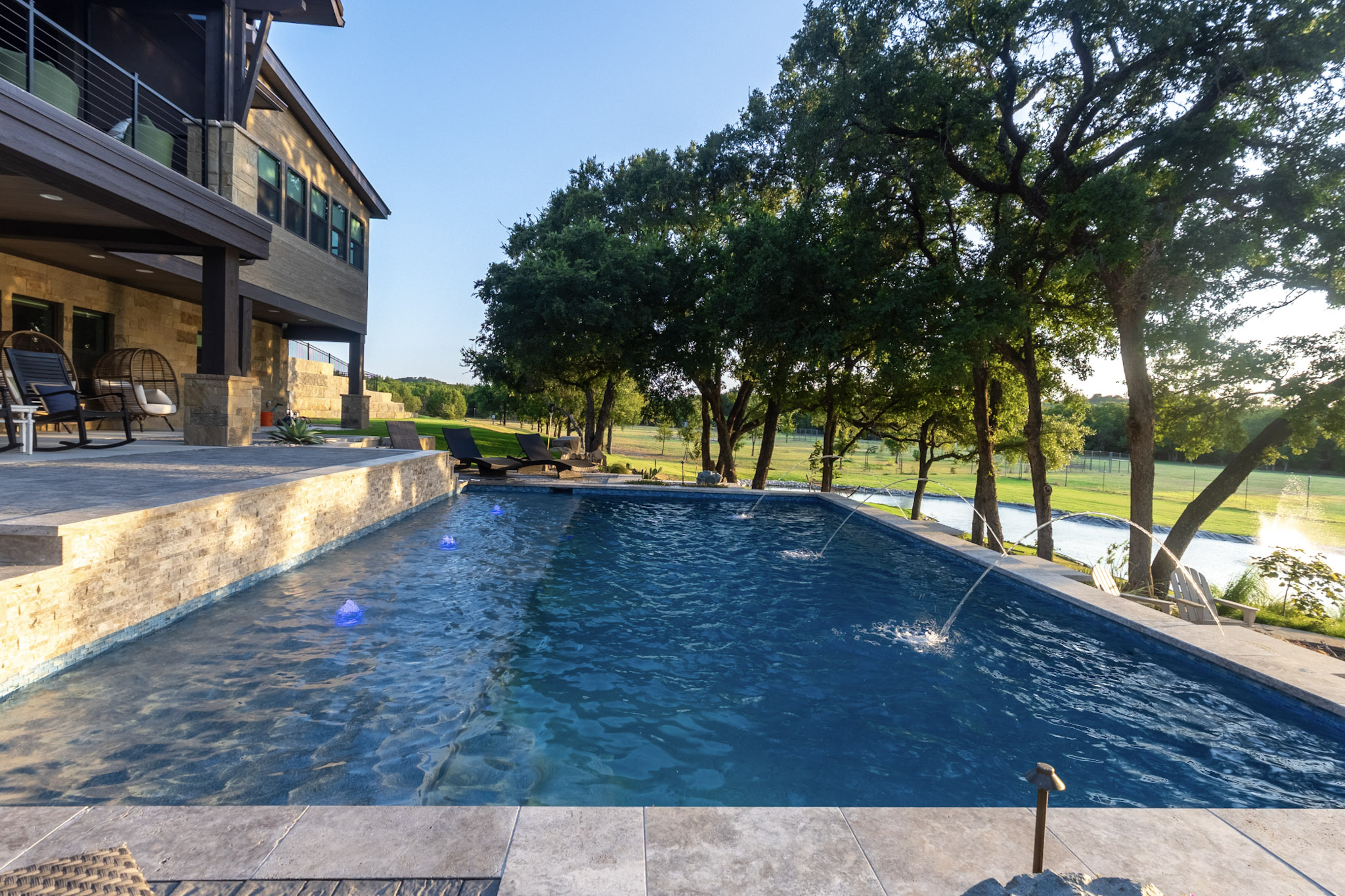 Pool with three laminar jets overlooking trees and a ranch pond.