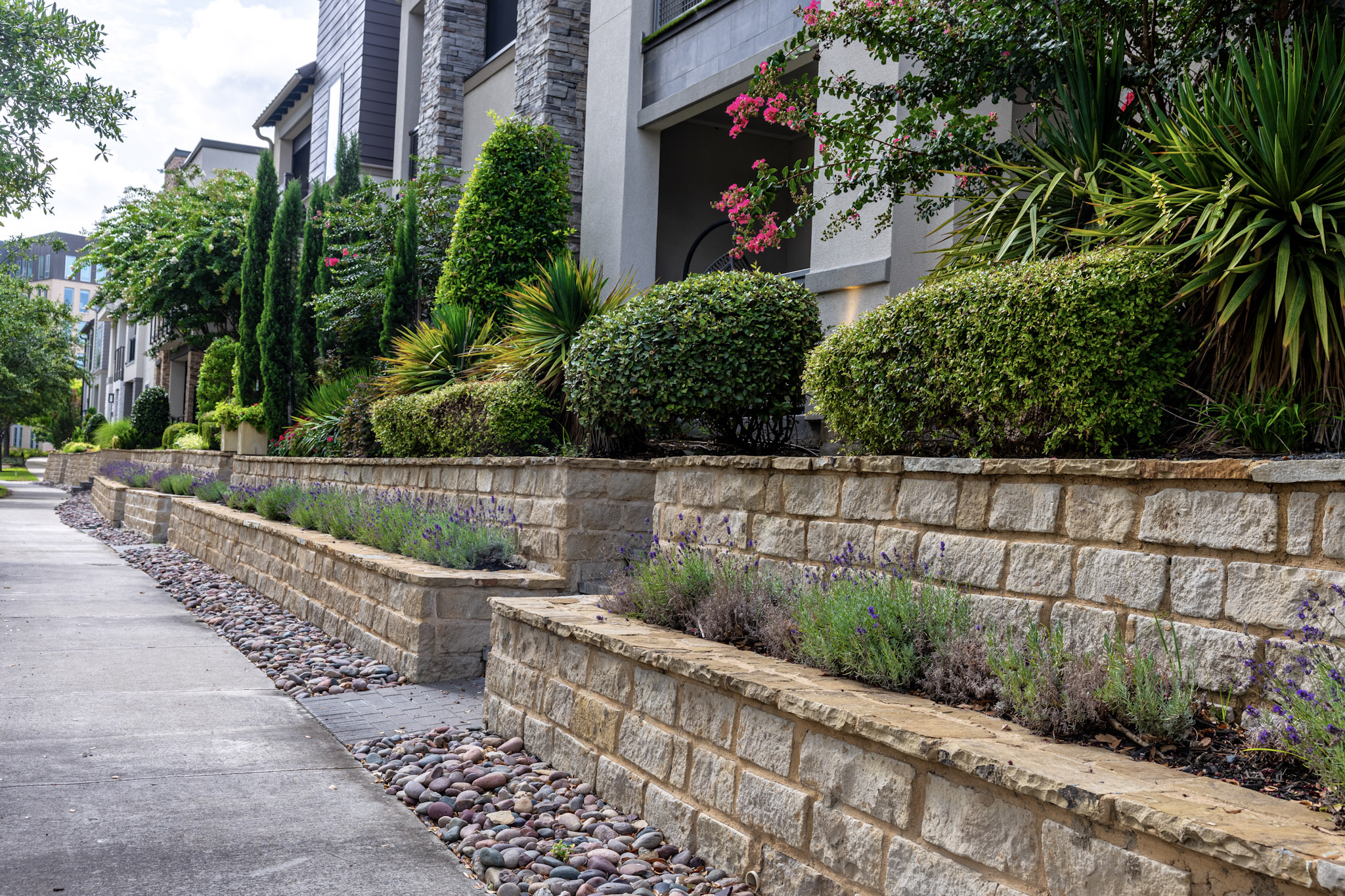 Tiered stone landscape walls with shrubs and purple flowering plants.