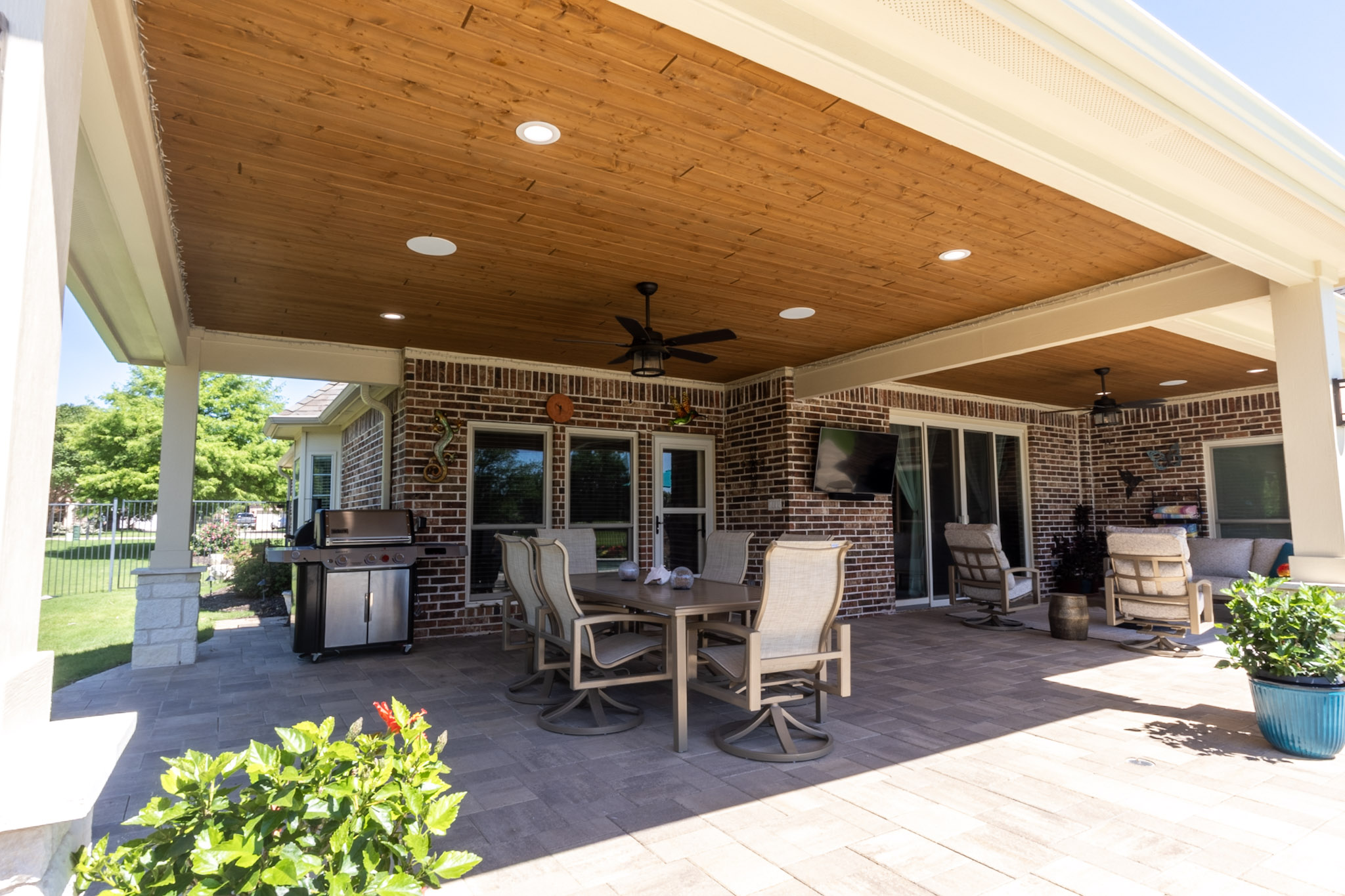 Outdoor lounge chairs beneath a wood patio ceiling with ceiling fans and pool visible beyond.