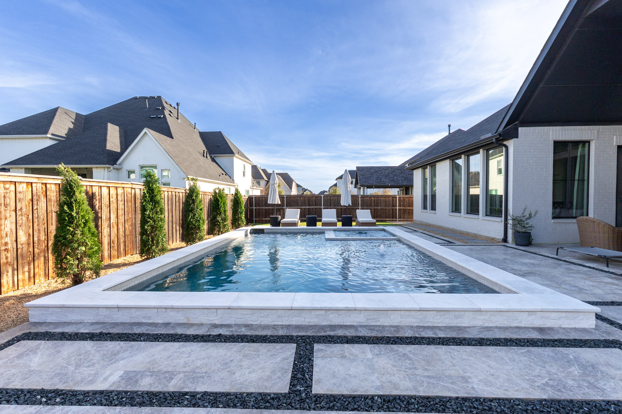 Wide rectangular pool with white coping, shallow ledge, spa and evergreen landscaping.