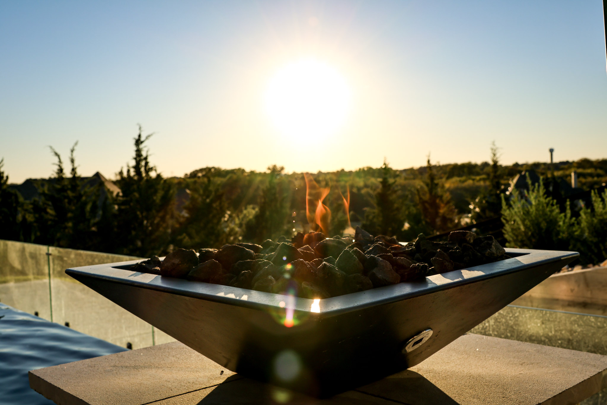 Raised fire bowl beside swimming pool with glass wind guard.