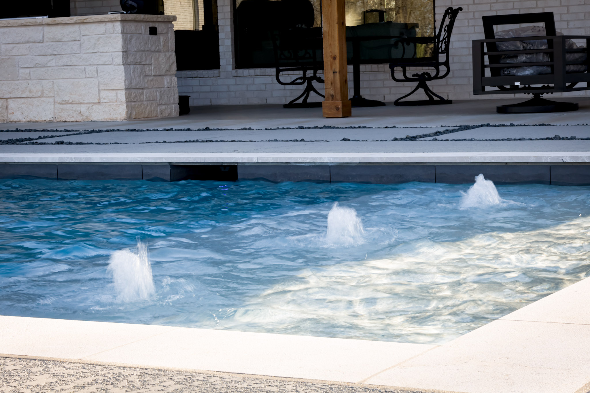 Three bubblers operating on a shallow tanning ledge in a rectangular swimming pool.