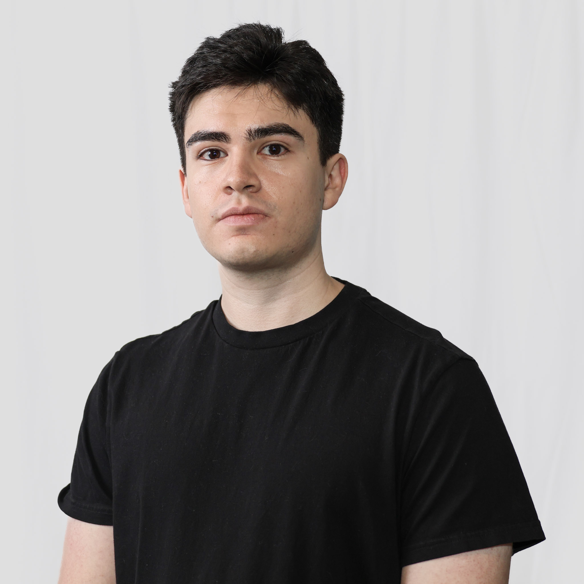 Joshua Flores wearing a black T-shirt with a neutral expression against a light studio background.
