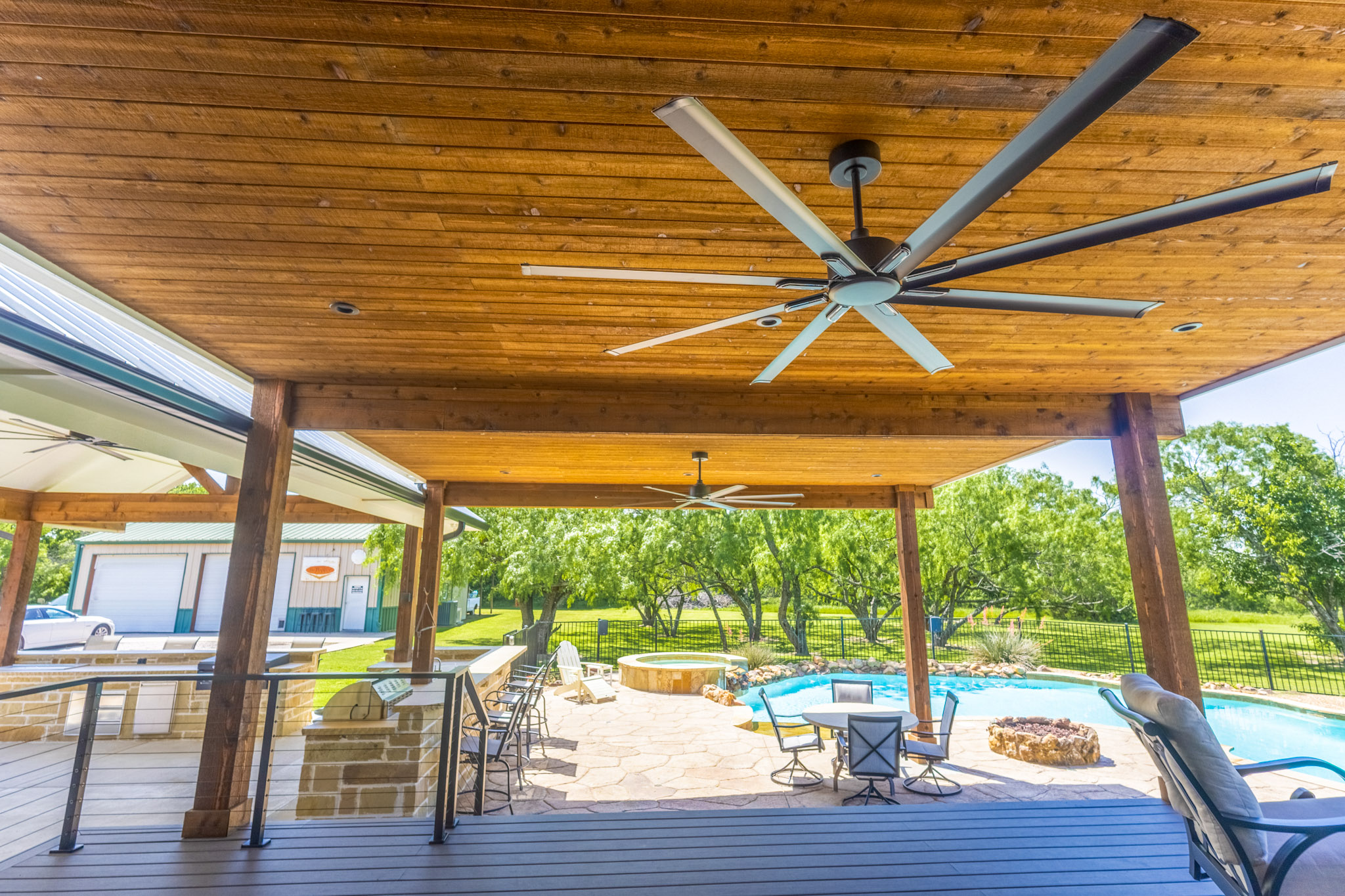 Covered composite deck with wood ceiling and ceiling fans overlooking a backyard pool.
