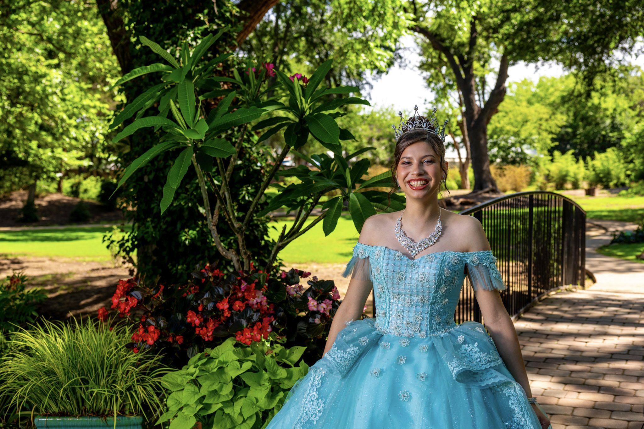 Quinceañera posing near flowers and a curved garden bridge