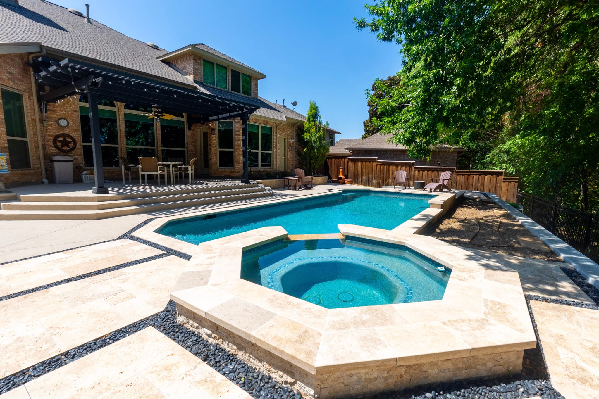 Raised geometric spa with light stone coping beside a large swimming pool and black pergola.