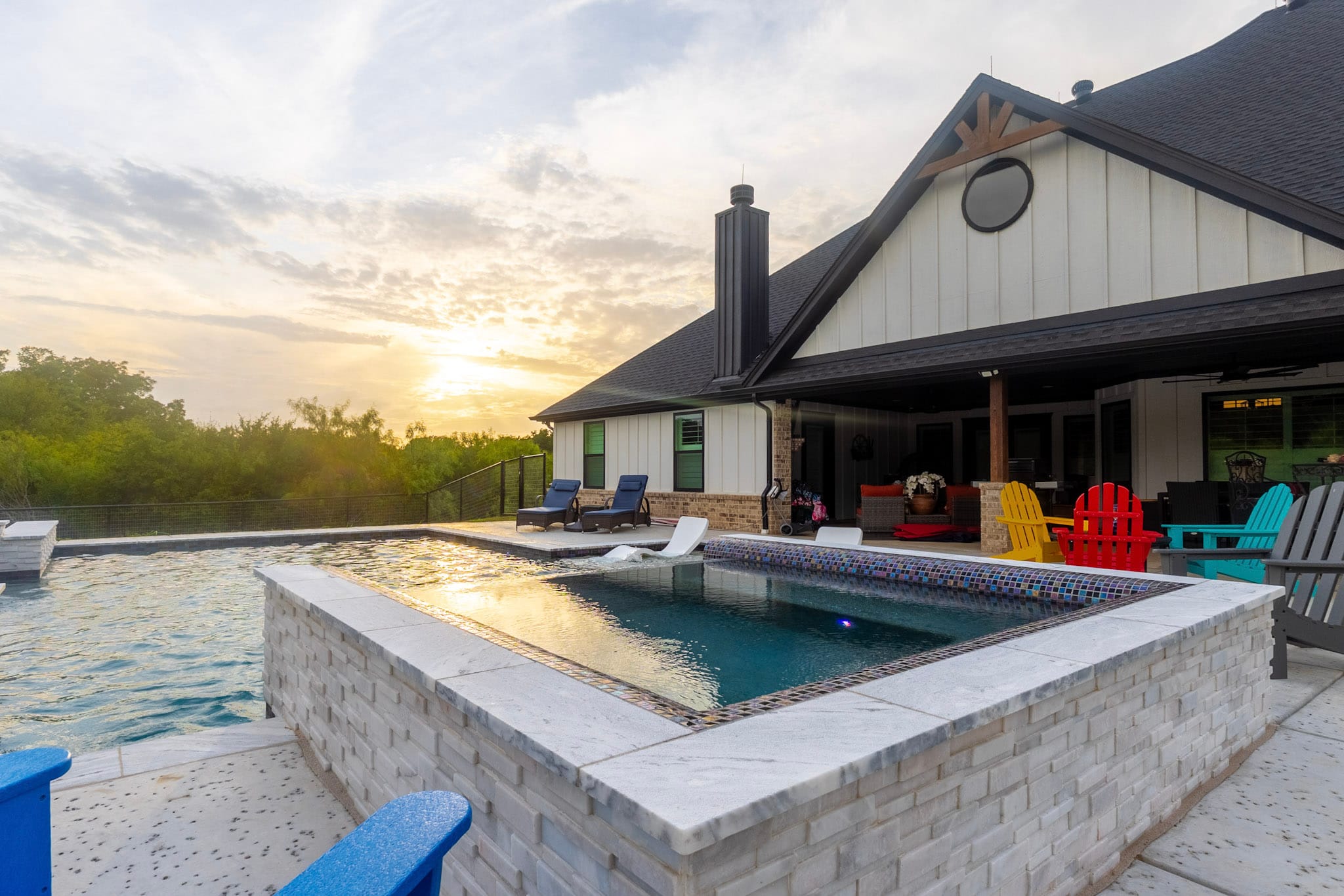 Raised stone spa beside a custom pool with a covered patio and colorful outdoor seating.