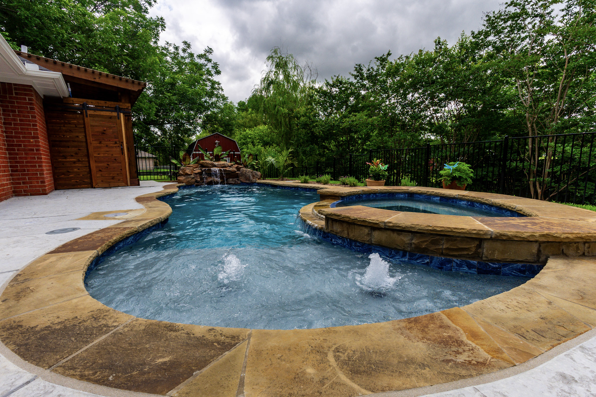 Wide freeform pool with raised spa, two bubblers and rock waterfall in the distance.