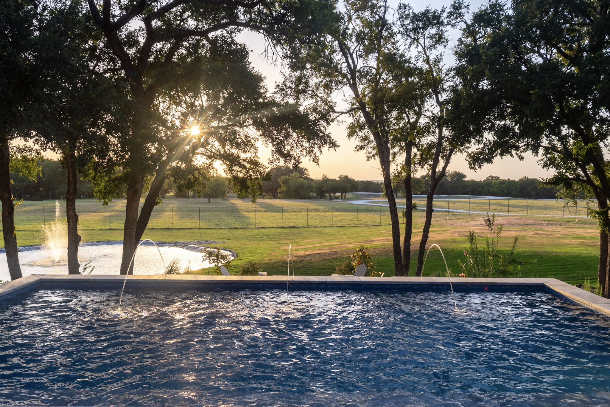Three laminar jets over a pool with ranch landscape at sunset.