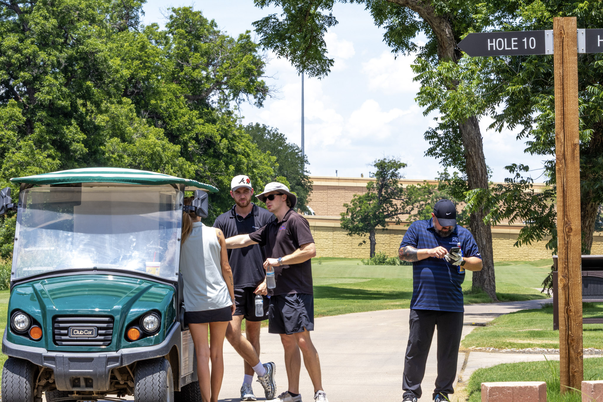 Golf event participants gathered near a golf cart and Hole 10 sign