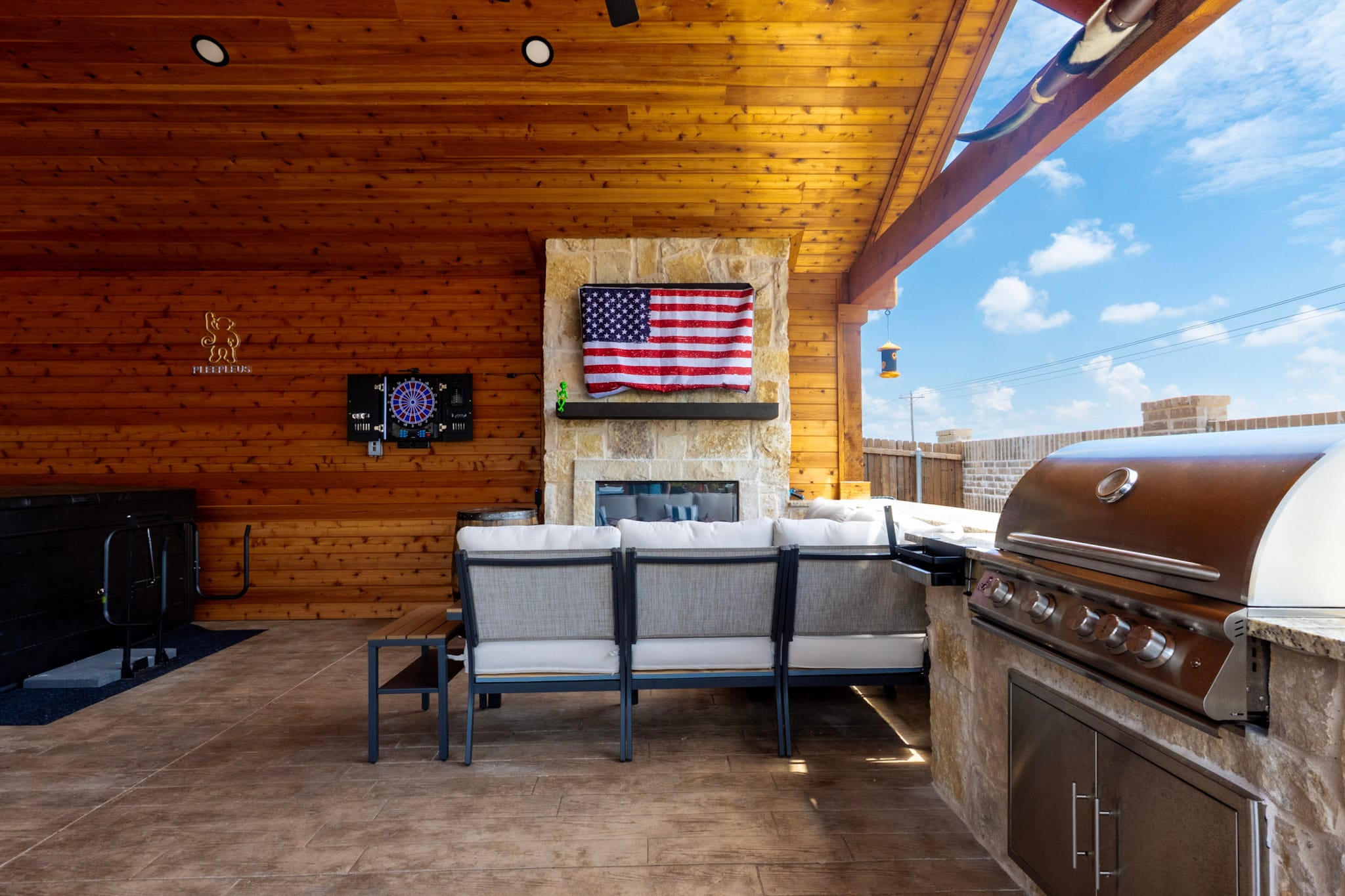 Covered patio with built-in grill, stone fireplace, sectional seating and wood ceiling.