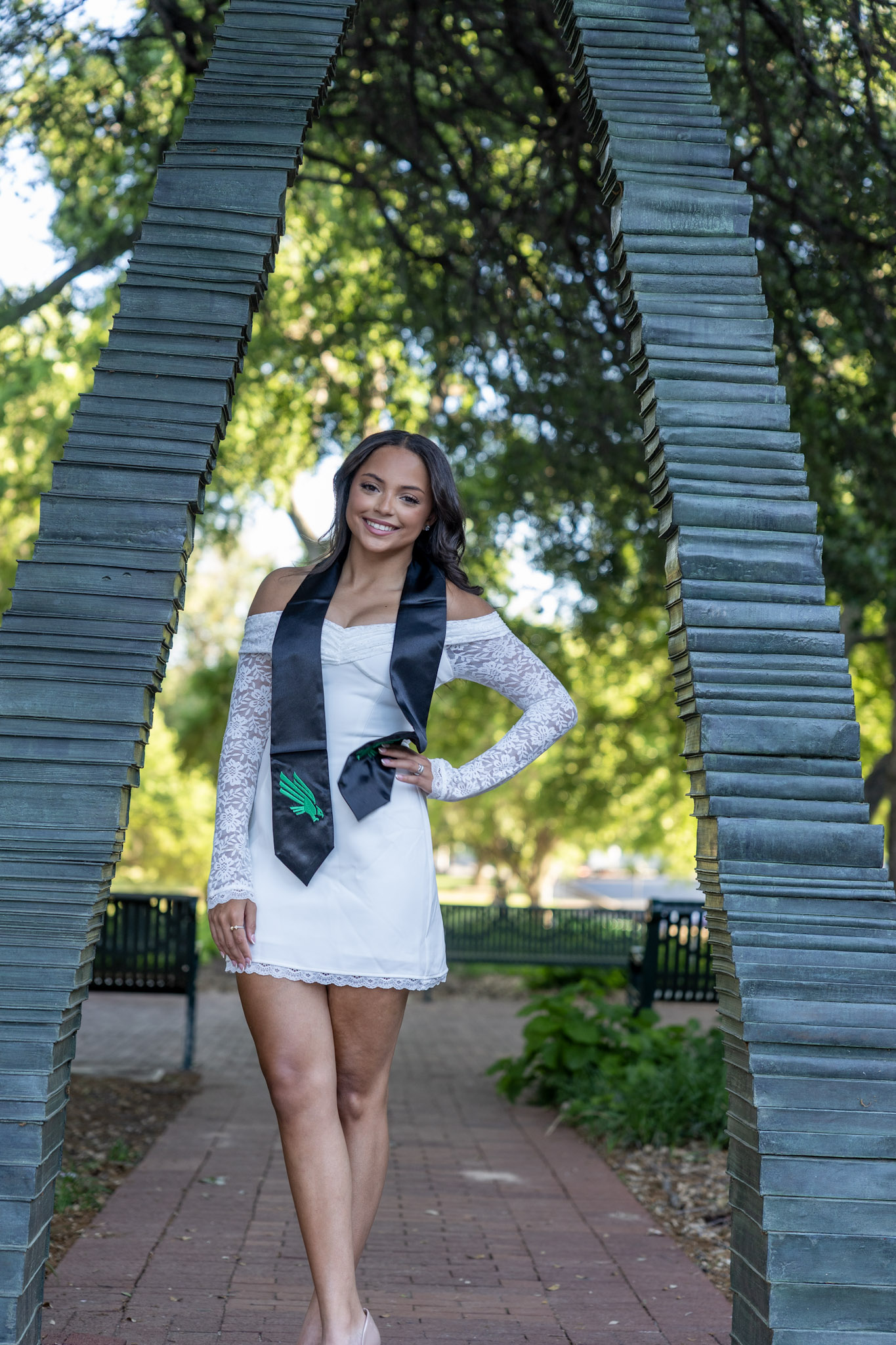 UNT graduate posing beneath a large outdoor arch sculpture