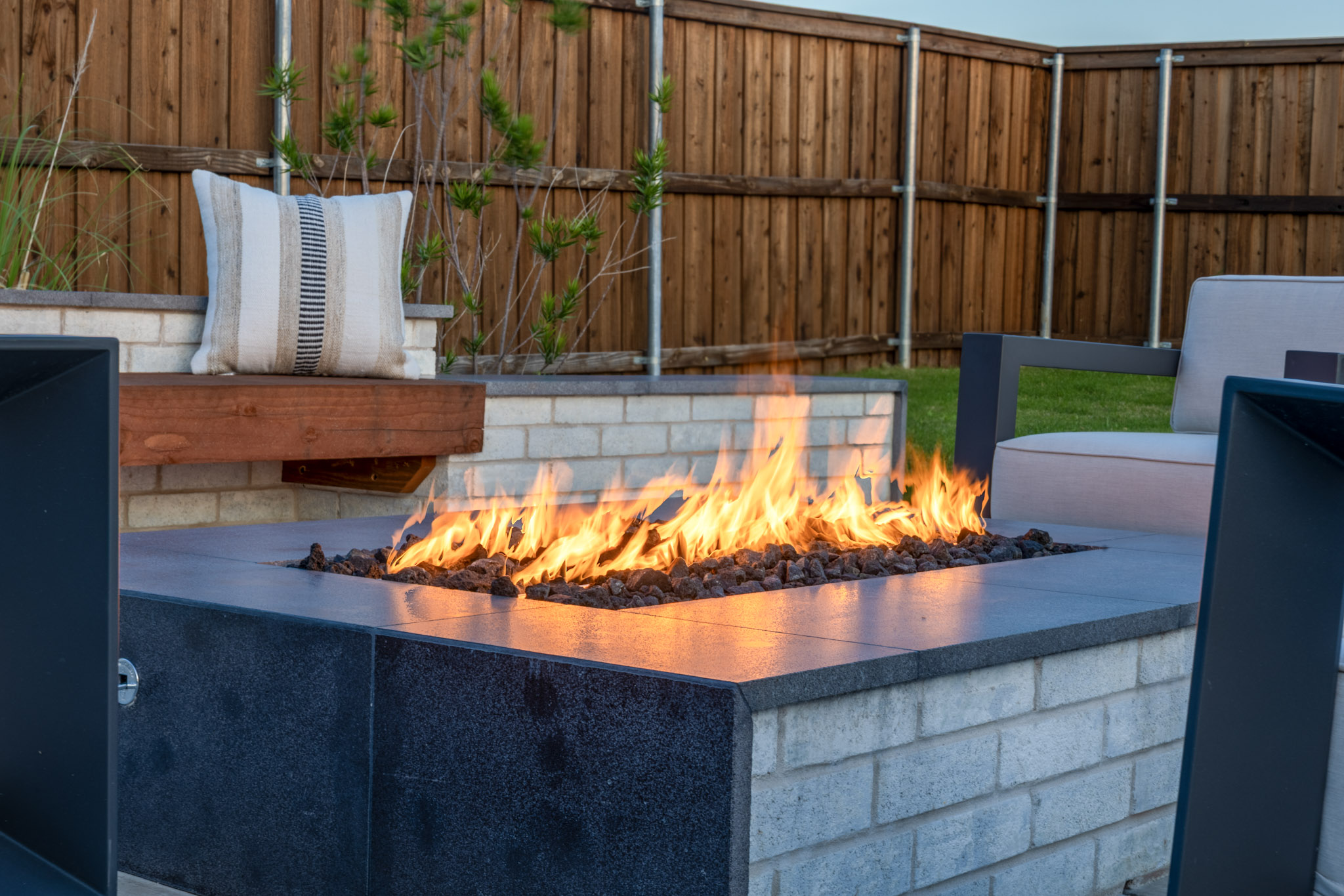 Linear outdoor fire feature with built-in wood bench and masonry planter wall.