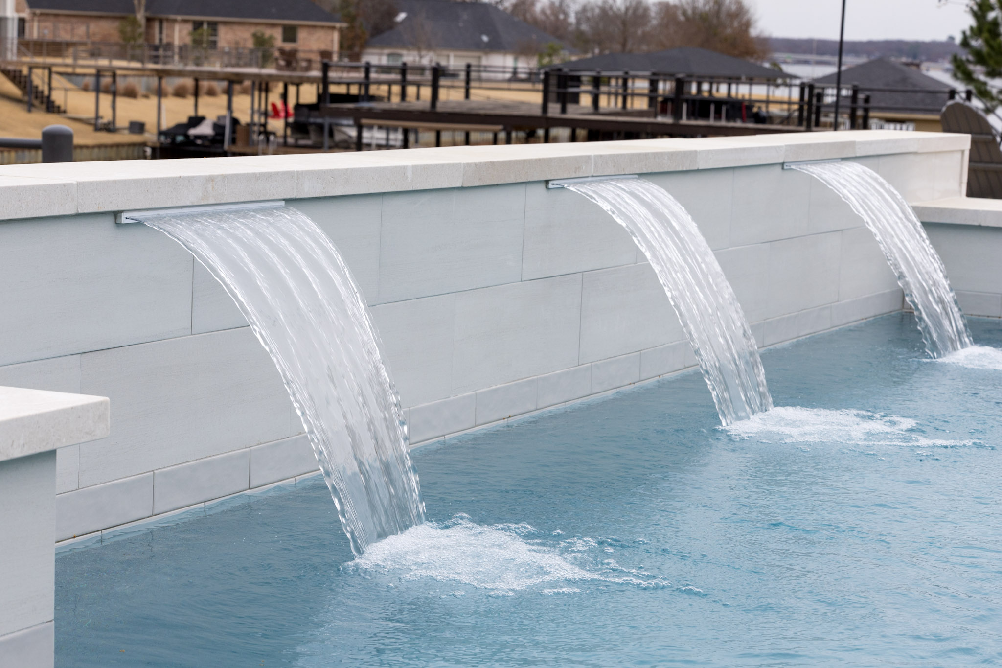 Three sheer descent water features flowing from a raised pool wall into blue water.