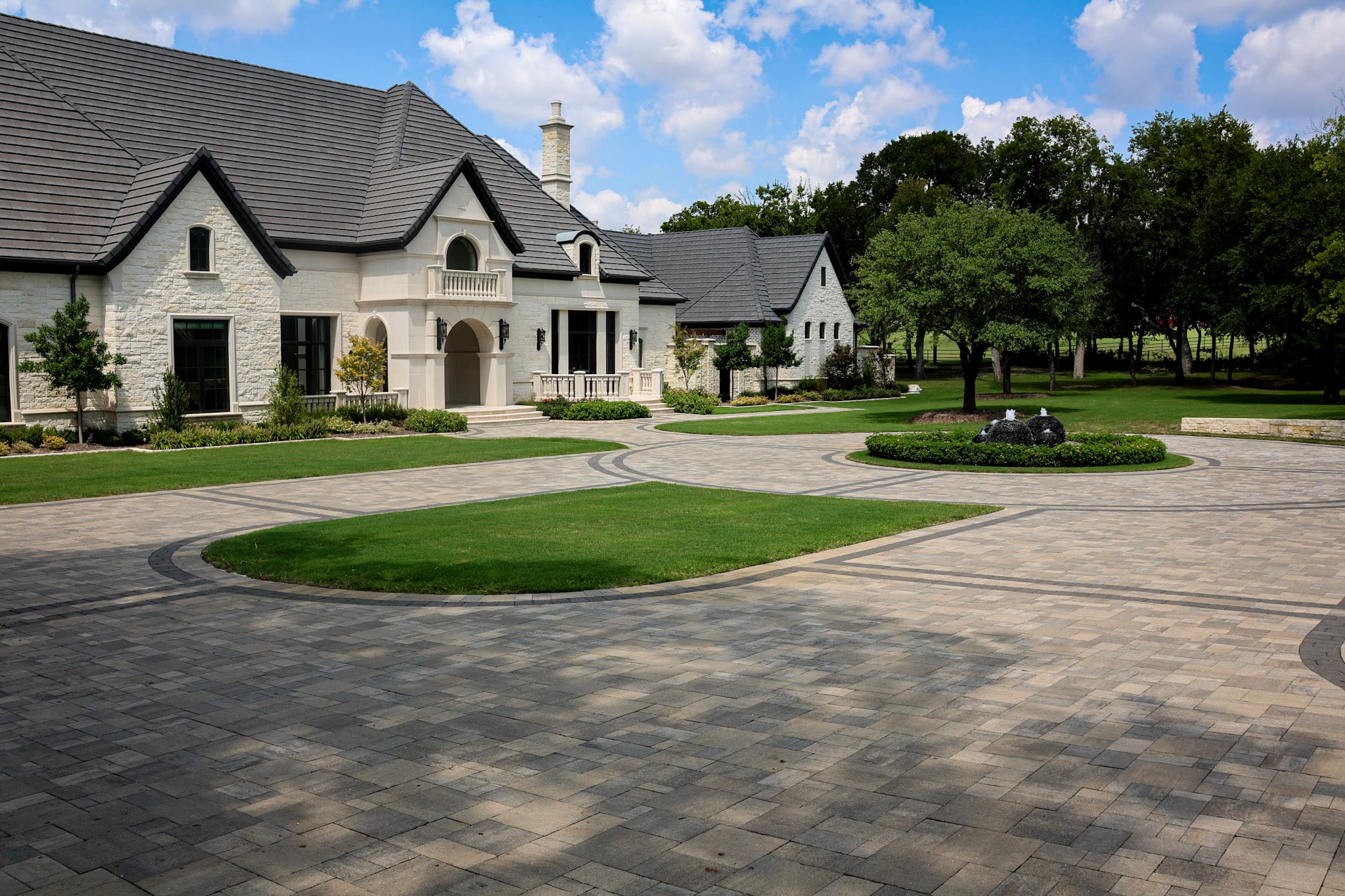 Wide Belgard paver driveway with dark border patterns leading toward a white stone home in Allen.