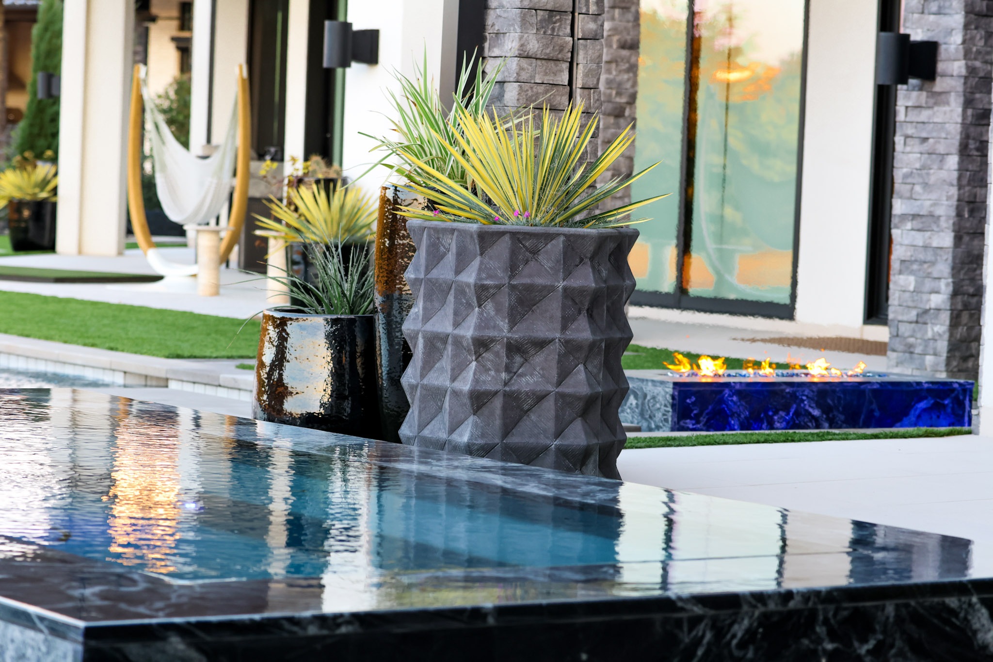 Modern planters beside reflective pool water and a linear fire feature.
