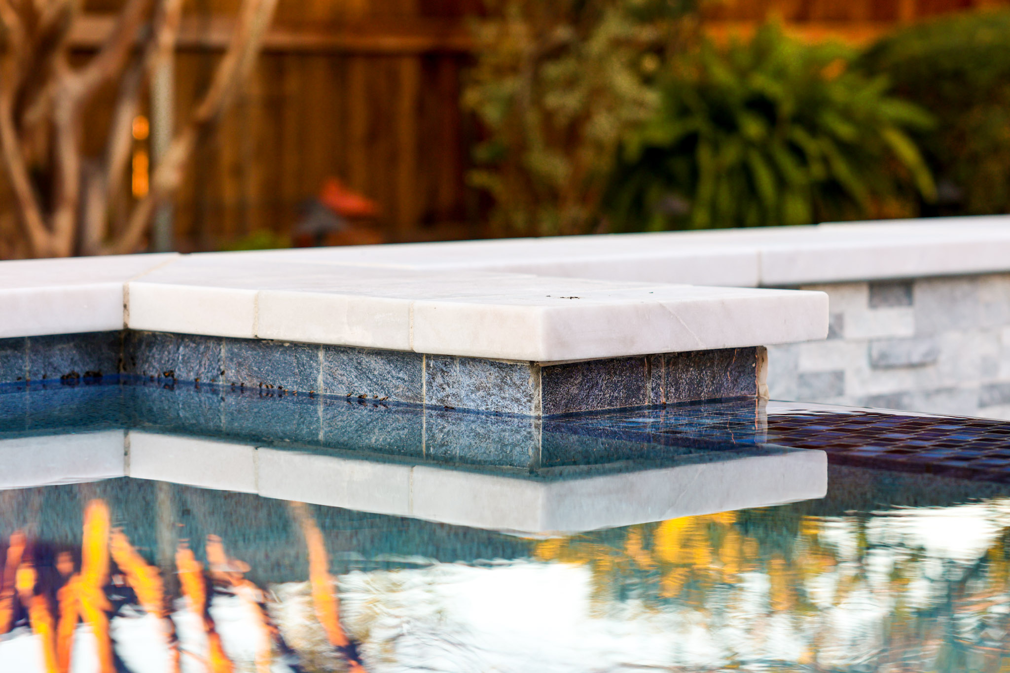 Close-up of white spa coping, dark waterline tile and water flowing between spa and pool.